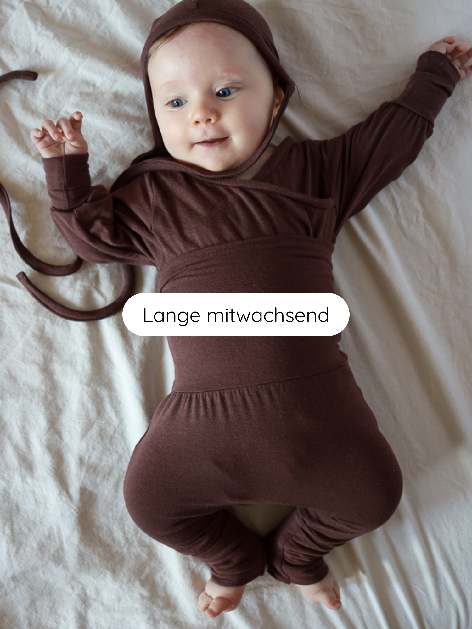 Säugling auf weicher Oberfläche in einem Babyknicker Bambusviskose Zartbitter, einem schokoladenbraunen, langärmligen Overall mit passender Haube, der mit dem Kind mitwächst.