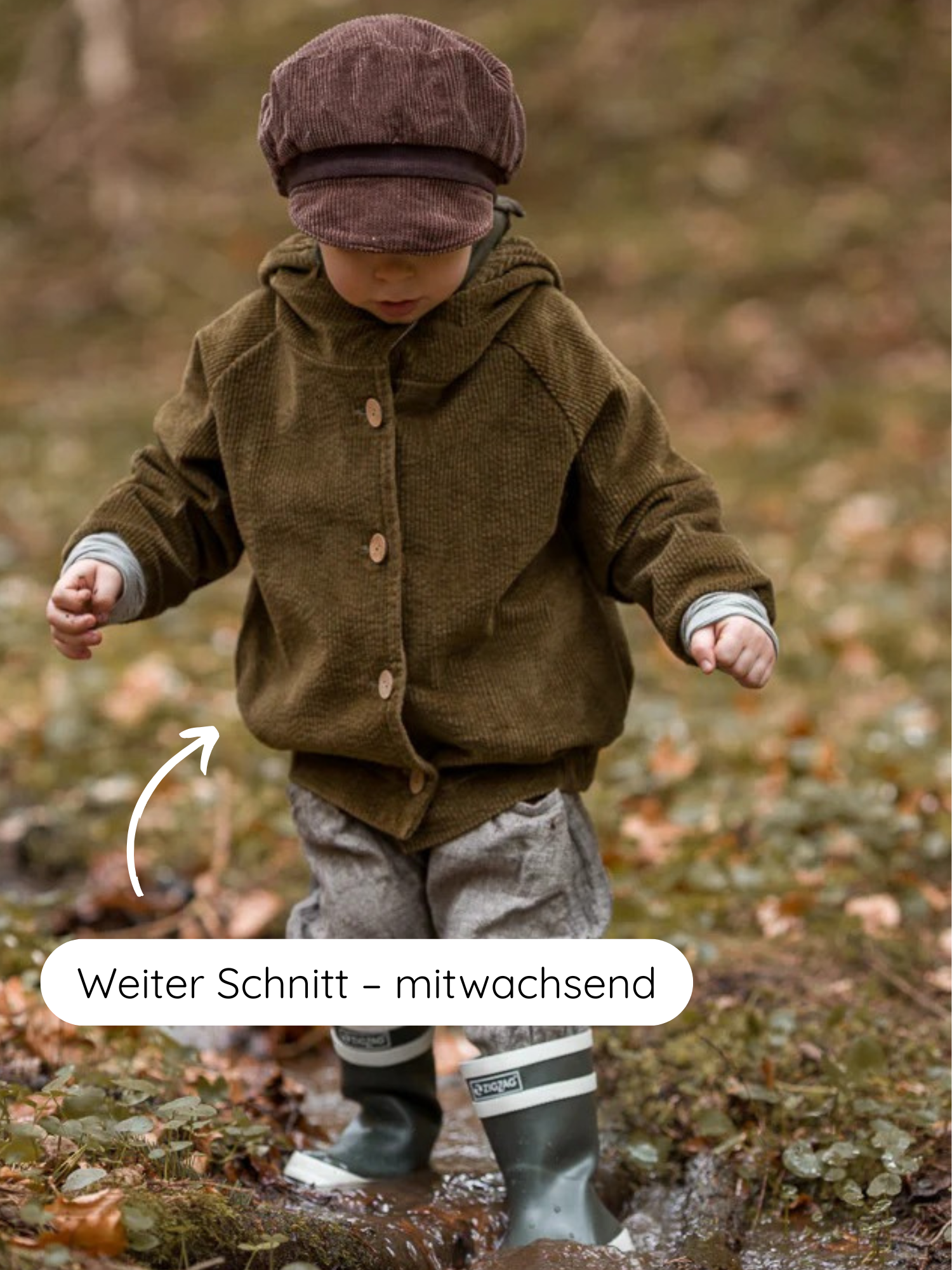 Ein Kind trägt die Wichteljacke Breitcord Stretch - Kiwi mit weiterem Schnitt und süßer Wichtelkapuze, die durch Ringel-Armbündchen mitwächst, während es durch eine Pfütze im Wald springt.
