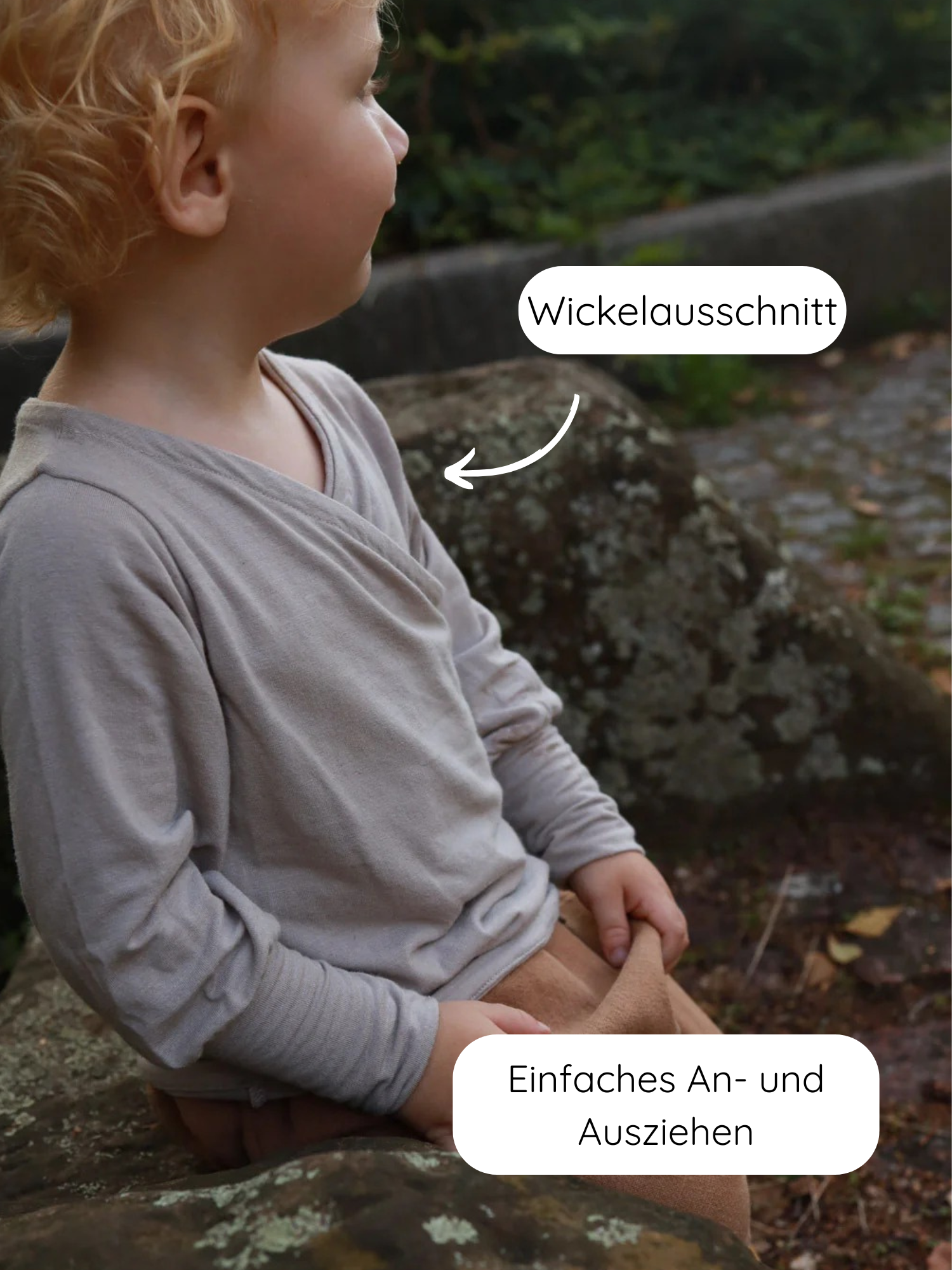 Kleinkind auf einem Stein trägt das Wickelshirt aus Kaschmir-Mix - Sand mit Wickelausschnitt, ideal für einfaches An- und Ausziehen. Passende, locker sitzende Hose aus dem gleichen weichen Material.