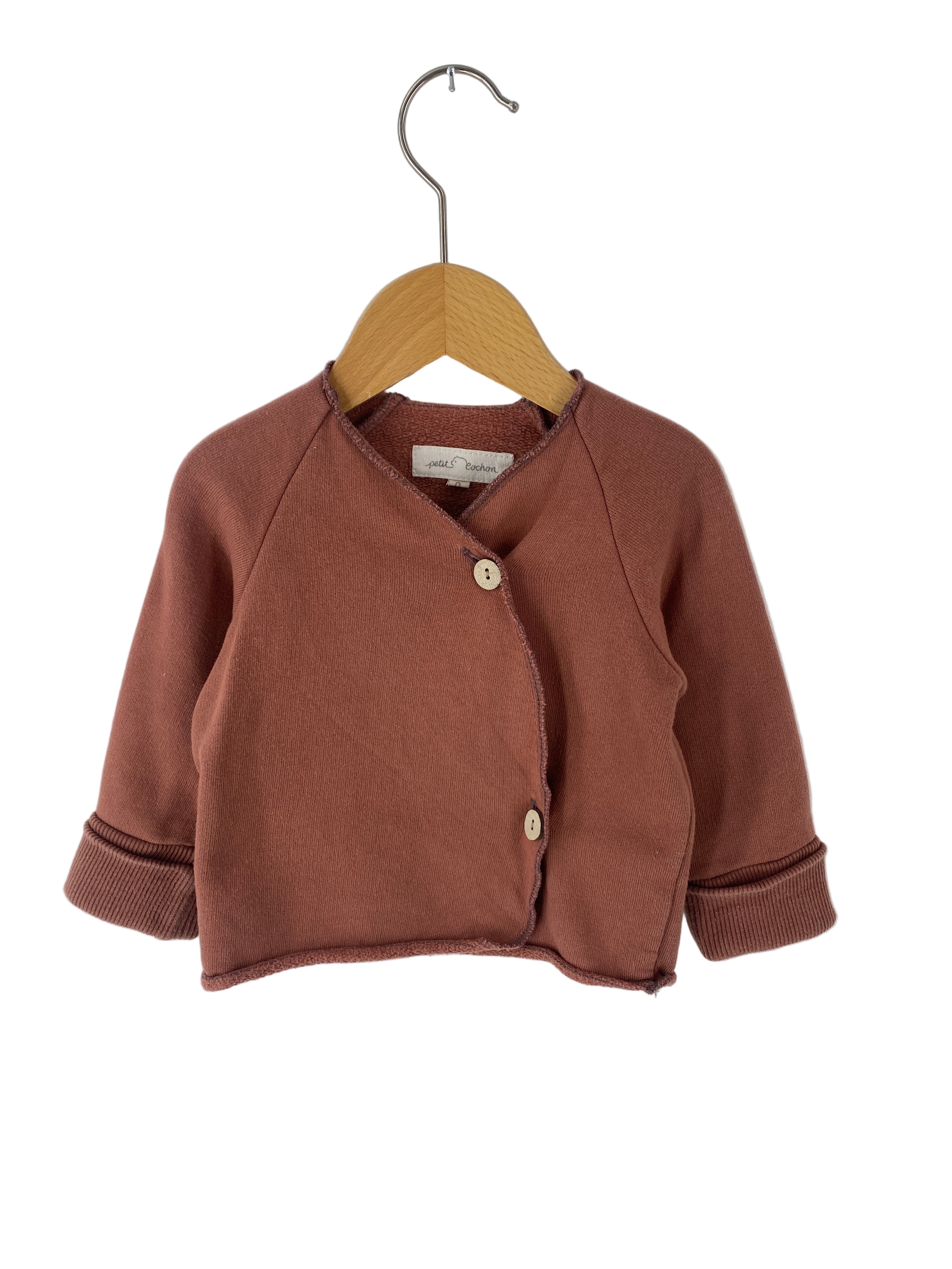 Kopie Schlüttli Bio-Sweat Zimt Gr 6M: Kleiner Langarm-Cardigan mit zwei Holzknöpfen, ausgestellt auf einem Holzkleiderbügel vor weißem Hintergrund. Zustand: sehr gut.