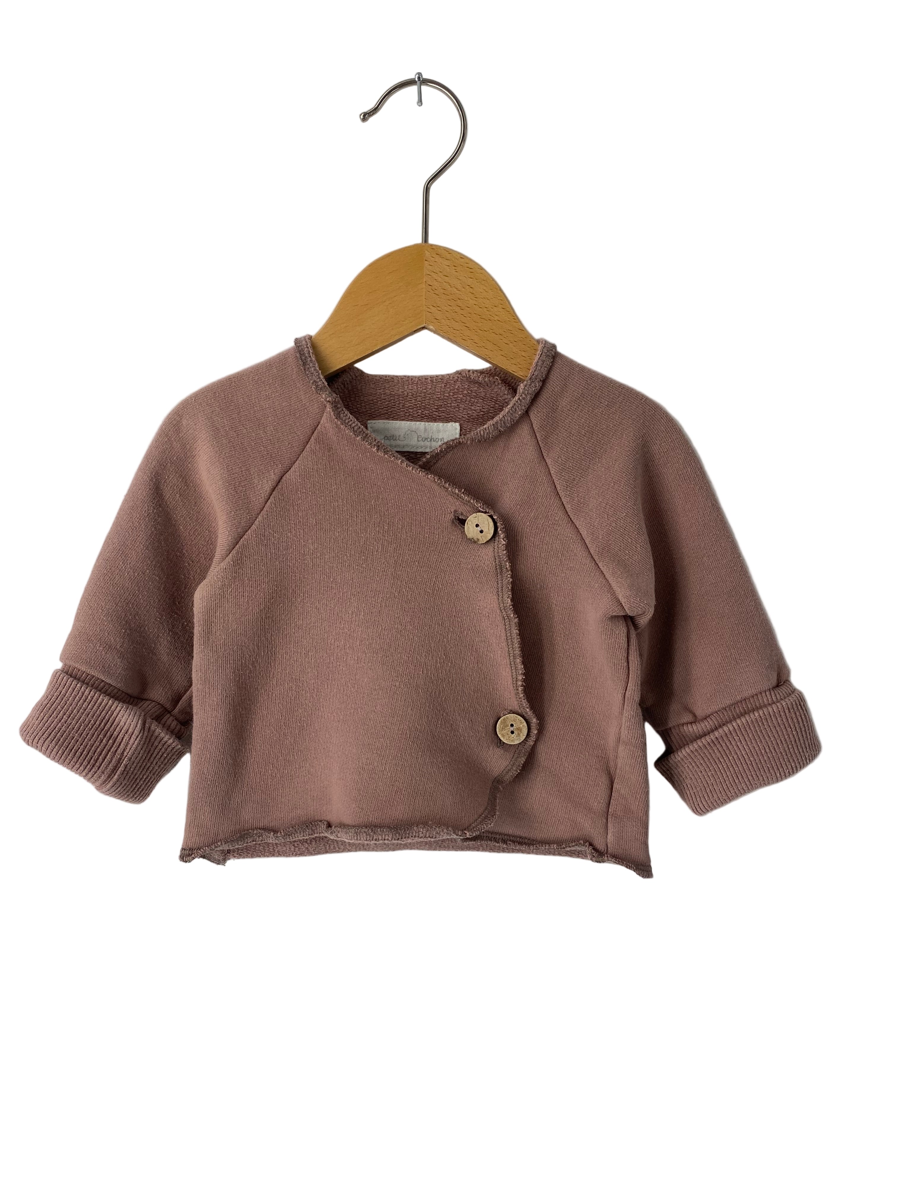 Loopbody Bambusviskose Salbei Gr 0M: Kleiner Kinder-Cardigan mit asymmetrischem Verschluss, langen Ärmeln, zwei runden Holzknöpfen und rohen Kanten, präsentiert auf einem Holzkleiderbügel vor weißem Hintergrund. Zustand: neu.
