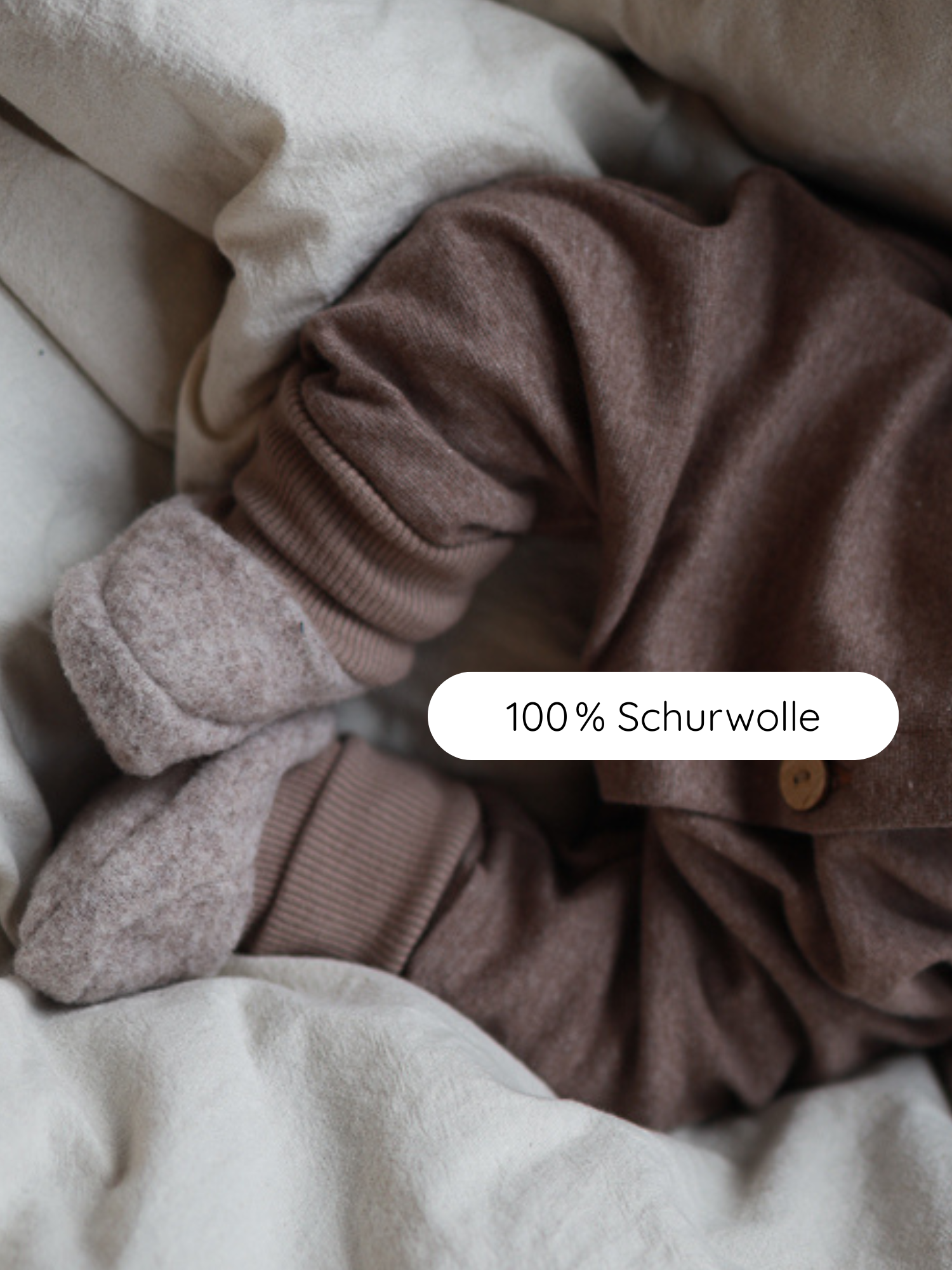 Nahaufnahme von Babybooties Merino Wollfleece - Hafer, an Babys Füßchen auf hellem Bettzeug. Die Booties aus 100% Schurwolle sind weich, flexibel und passen sich Babys Füßen an, ohne einzuschnüren.