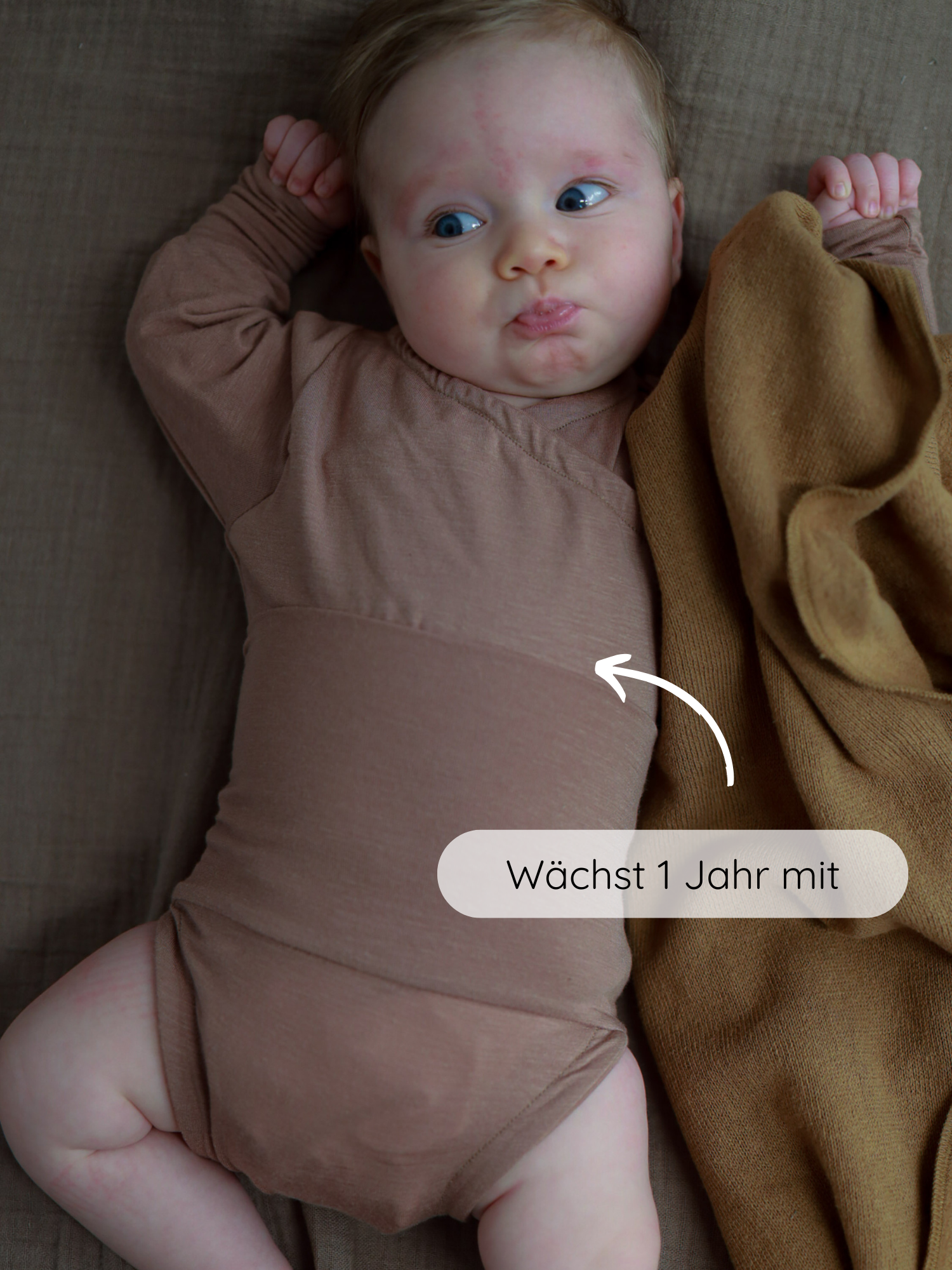 Baby in einem Loopbody Kaschmir-Mix - Puder, der auf einer braunen Fläche liegt. Der Body wächst ein Jahr mit, ohne Knöpfe, mit umschließendem Loop für Wärme und einfache Handhabung.