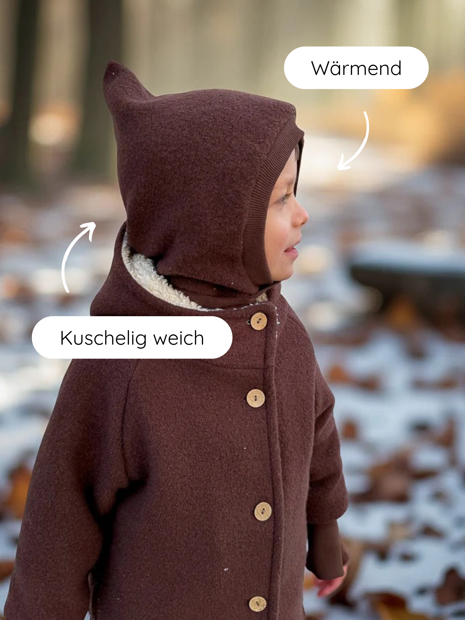 Kleinkind im Freien trägt Schlupfmütze Wollwalk - Schoko mit spitzer Kapuze und Kuschelkragen, umgeben von Schneefall und Laub. Kapuze „Wärmend“, Kragen „Kuschelig weich“ laut Bildüberlagerung.