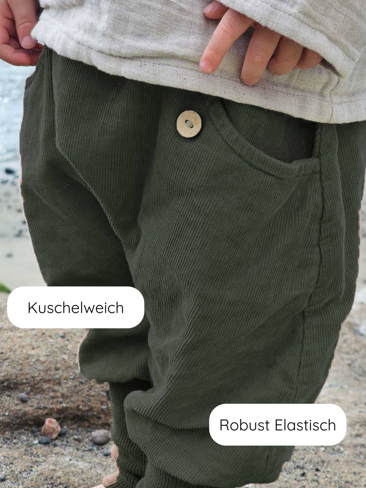 Kleinkind in olivegrüner Knickerbocker Feincord - Avocado mit elastischem Bund und Holzknopf, steht am Ufer. Labels „Kuschelweich“ und „Robust Elastisch“ zeigen die weichen, flexiblen Eigenschaften der Hose.