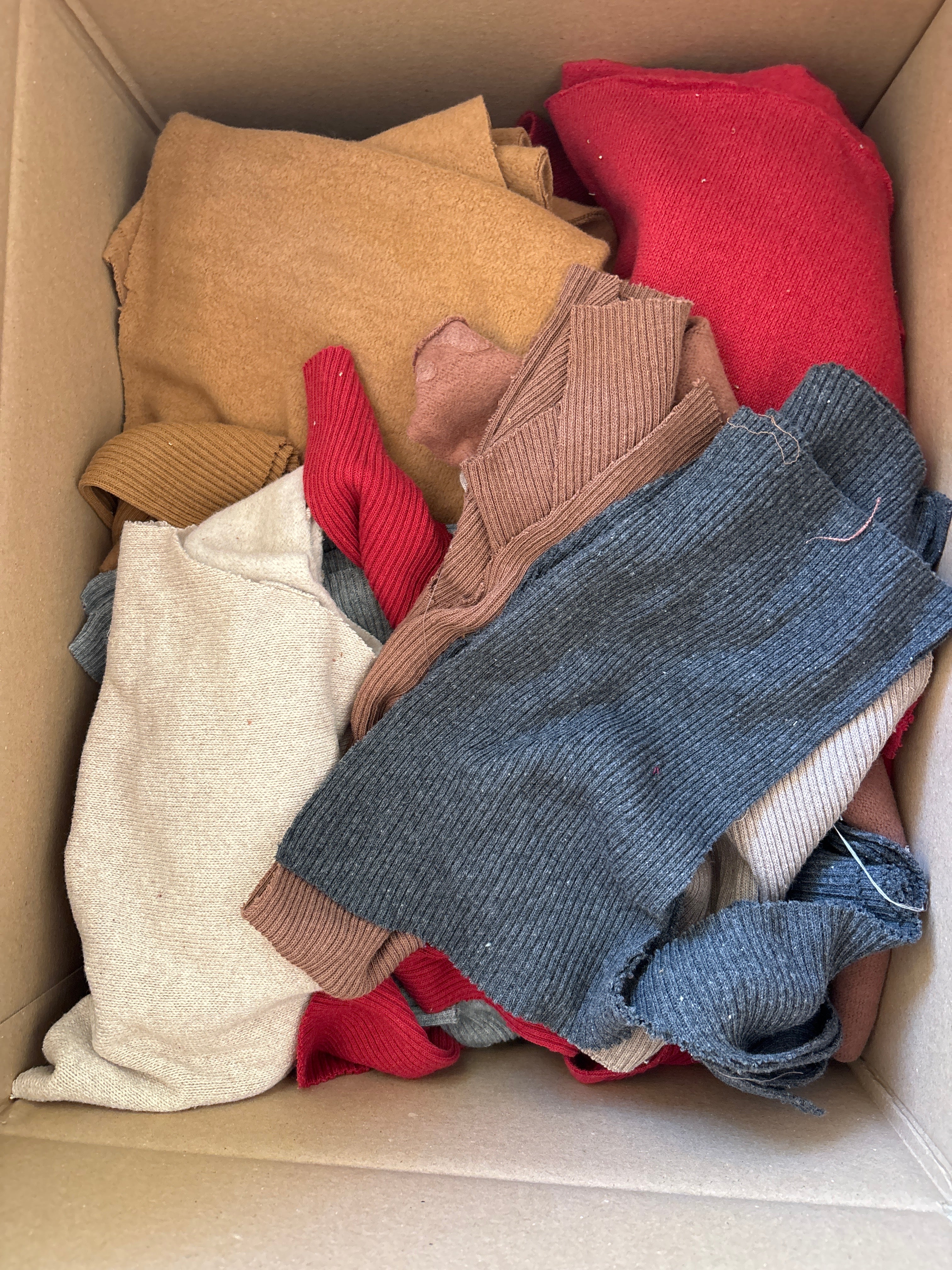Ca. 2 kg Stoffreste Strick aus recycelter Baumwolle in einem Karton, mit unterschiedlichen Strickarten wie Ripp- und Glattstrick. Unterschiedliche Breiten zwischen 10-30 cm sind sichtbar.
