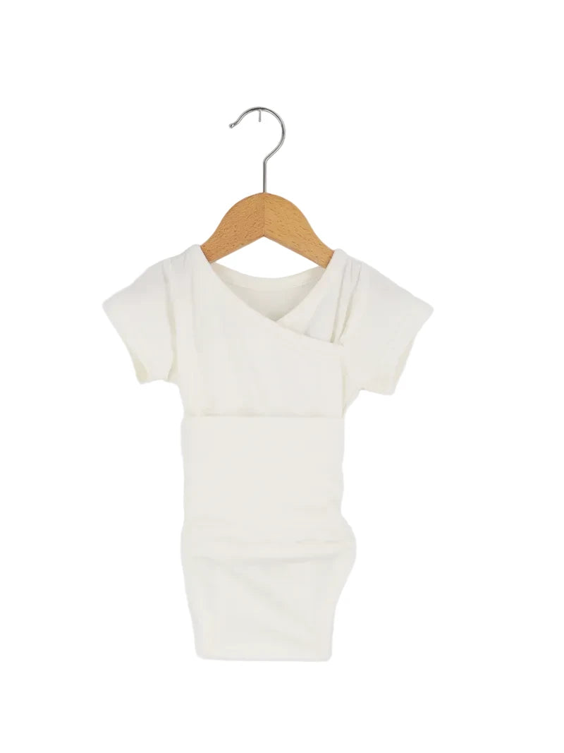 Der Kurzarm Loopbody Bambusviskose Natur Gr 1Y, ein schlichtes weißes Baby-Body mit kurzen Ärmeln, hängt an einem Holzkleiderbügel. Zustand neu, aber mit kleinem Fleck am Ärmel.