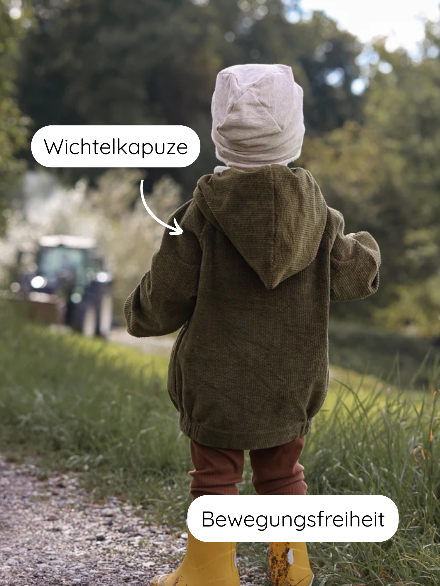 Ein Kind trägt die Wichteljacke Breitcord Stretch - Kiwi mit Wichtelkapuze, kombiniert mit einer rosa Beanie, rostfarbenen Leggings und gelben Gummistiefeln, auf einem Kiesweg am Feldrand.