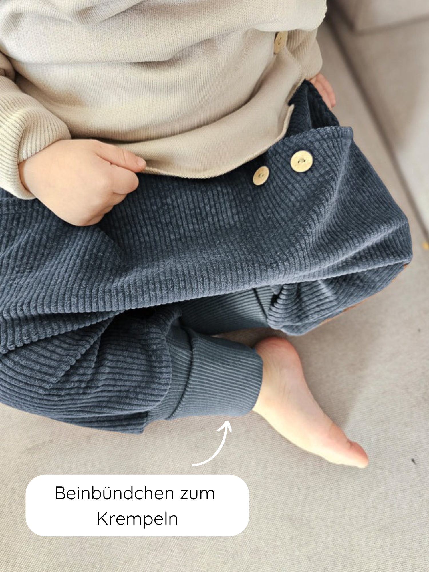 Kleinkind trägt Knickerbocker Breitcord - Jeansblau mit krempelbaren Beinbündchen und beiger Stricktop, zeigt eine Hand und einen Fuß. Ideal für Alltag, robust und bequem für maximale Bewegungsfreiheit.