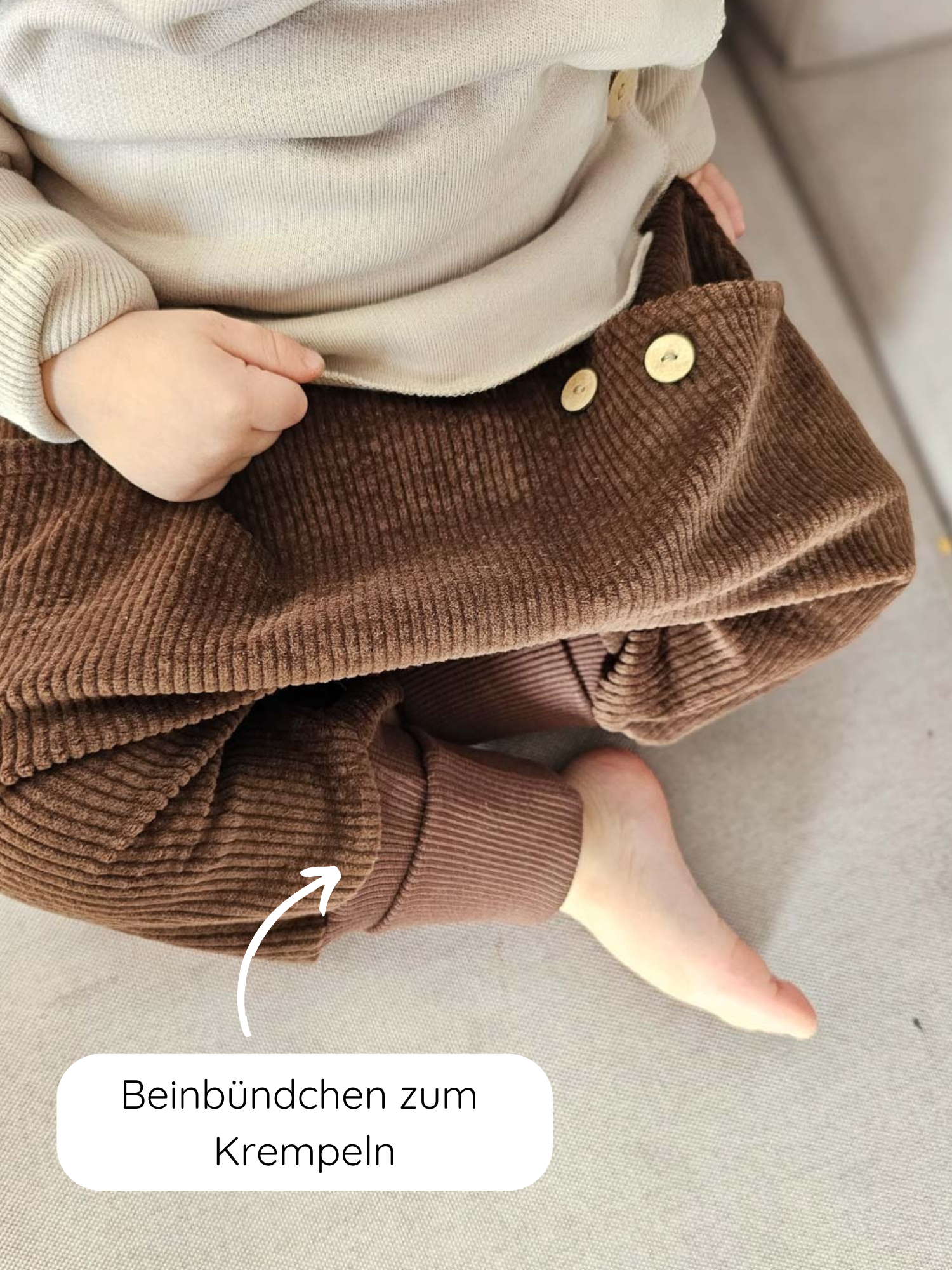 Knickerbocker Breitcord - Schoko: Kind trägt beige Pullover und braune, weiche Cordhose mit goldfarbenen Knöpfen. Hochrollbare Bündchen zeigen nackten Fuß, bieten Bewegungsfreiheit und Wachstumsflexibilität. Ideal für Alltagsabenteuer.