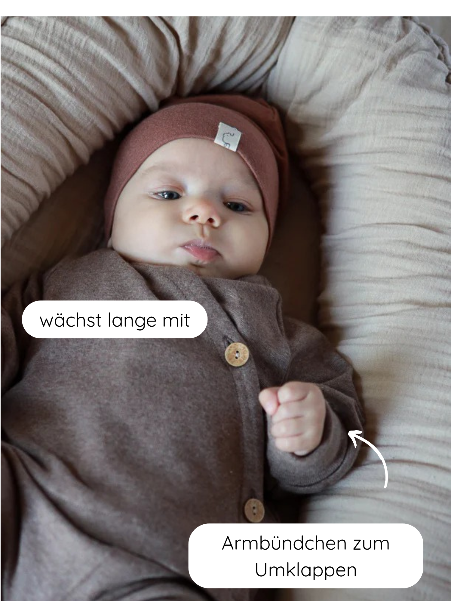 Ein Baby liegt in einem weichen Nest, trägt den Babyschlüttli Feinstrick - Praline Meliert, ein braunes Set mit Holzknöpfen und umklappbaren Armbündchen, das mitwächst.