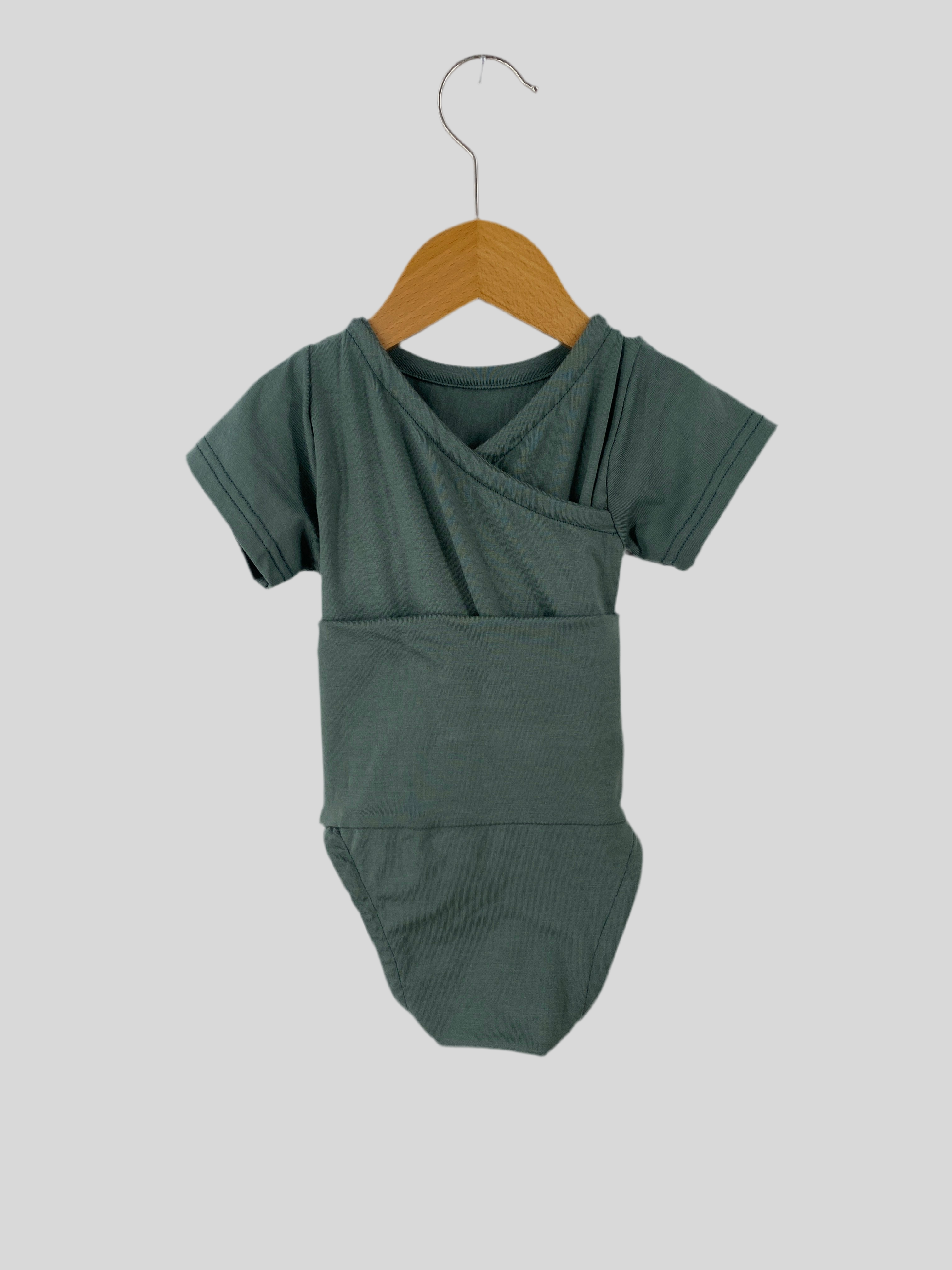 Kurzarm Loopbody Tencel Taube Gr 3M hängt an einem Kleiderbügel, zeigt die feine Verarbeitung und das weiche Material des neuen Babysuits, ideal für modische und bequeme Babykleidung.