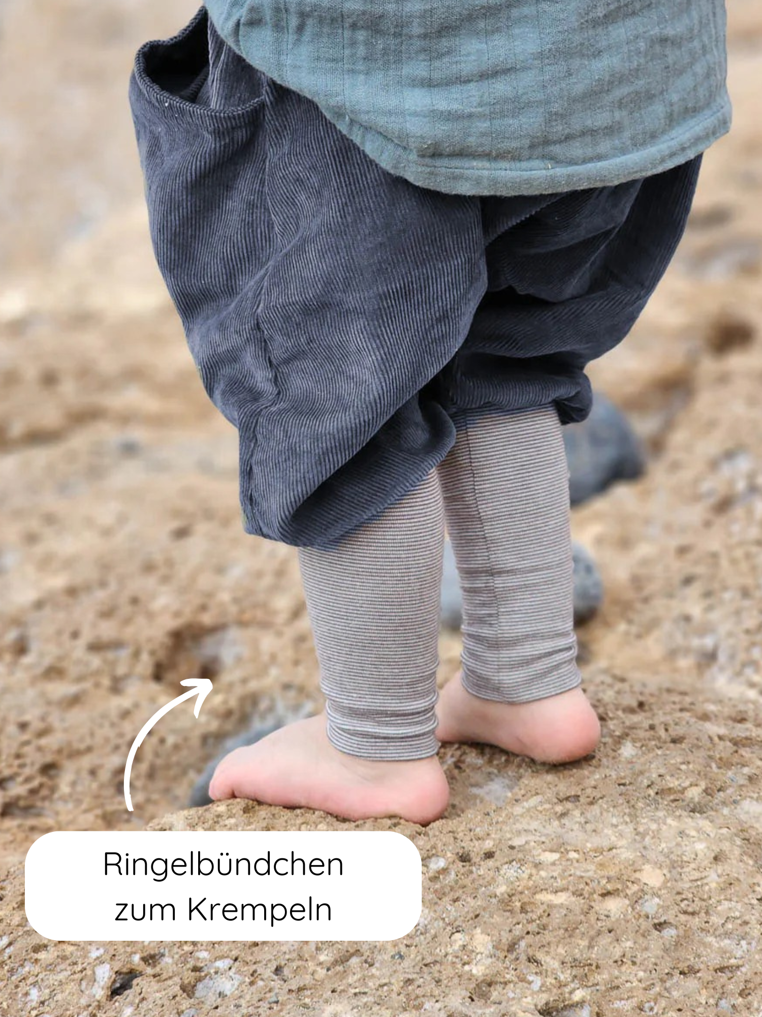 Knickerbocker Feincord Ringel - Blaubeere: Nahaufnahme von Kinderbeinen in grauen Cord-Haremshosen mit gestreiften, krempelbaren Bündchen auf sandigem Boden. Ringelbündchen zum Krempeln zeigt die umschlagbaren Bündchen.