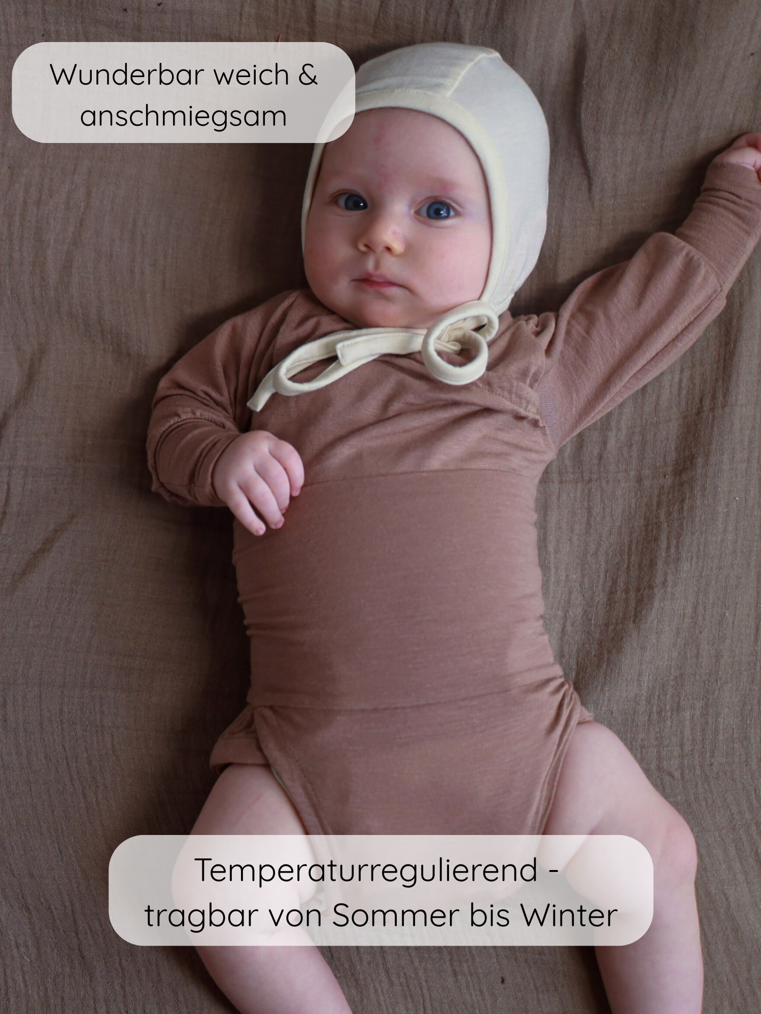Das Bild zeigt einen Säugling in einem Loopbody Kaschmir-Mix - Puder, der langärmelig ist. Der Body ist ohne Knöpfe und mit einer cremefarbenen Mütze kombiniert, auf einem braunen Stoffhintergrund.