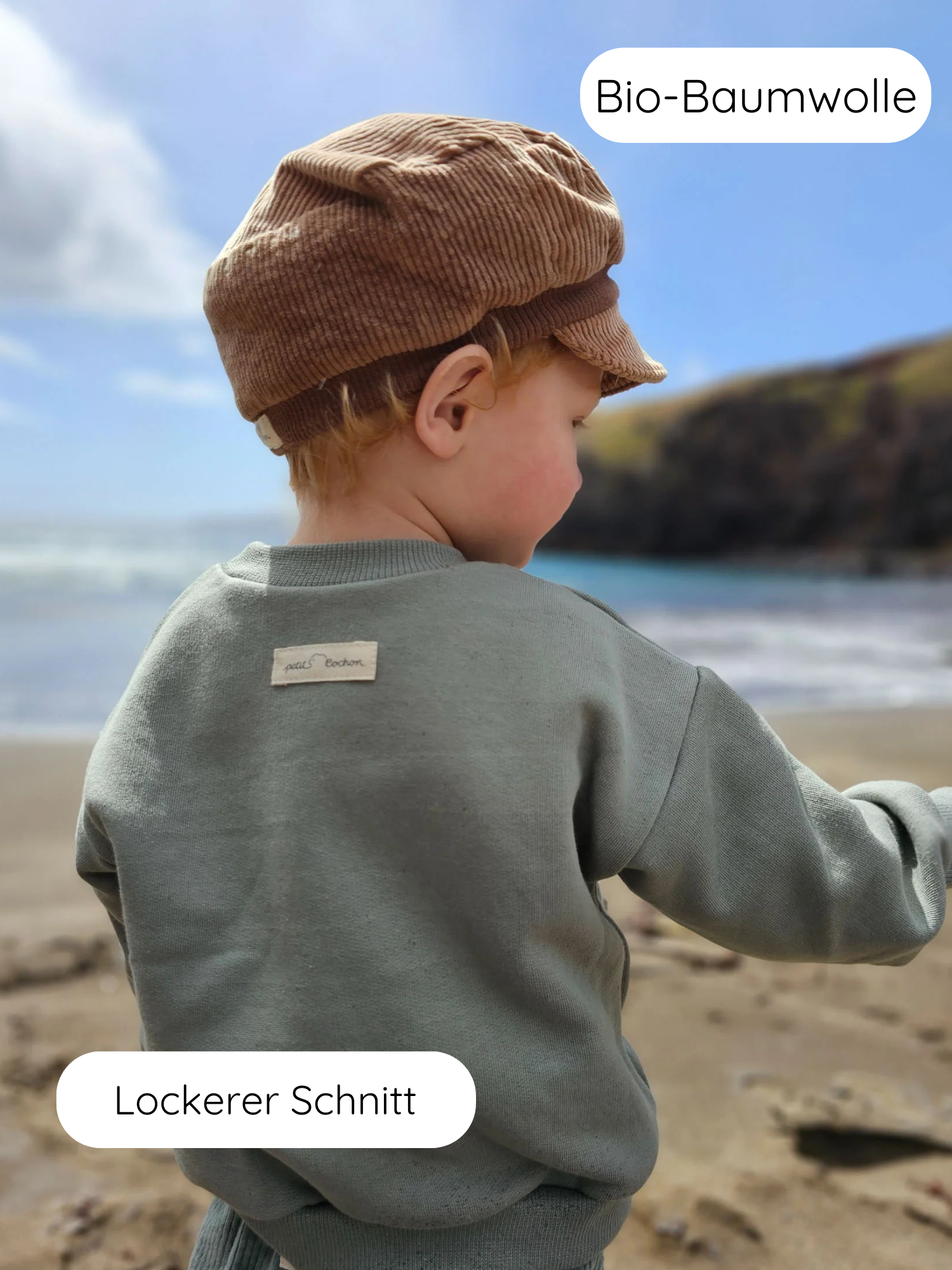 Ein Kind am Strand trägt den kuscheligen Pulli Bio-Sweat - Aqua aus Bio-Baumwolle mit lockerem Schnitt und Cordmütze, hervorgehoben durch Bio-Baumwolle und Lockerer Schnitt.
