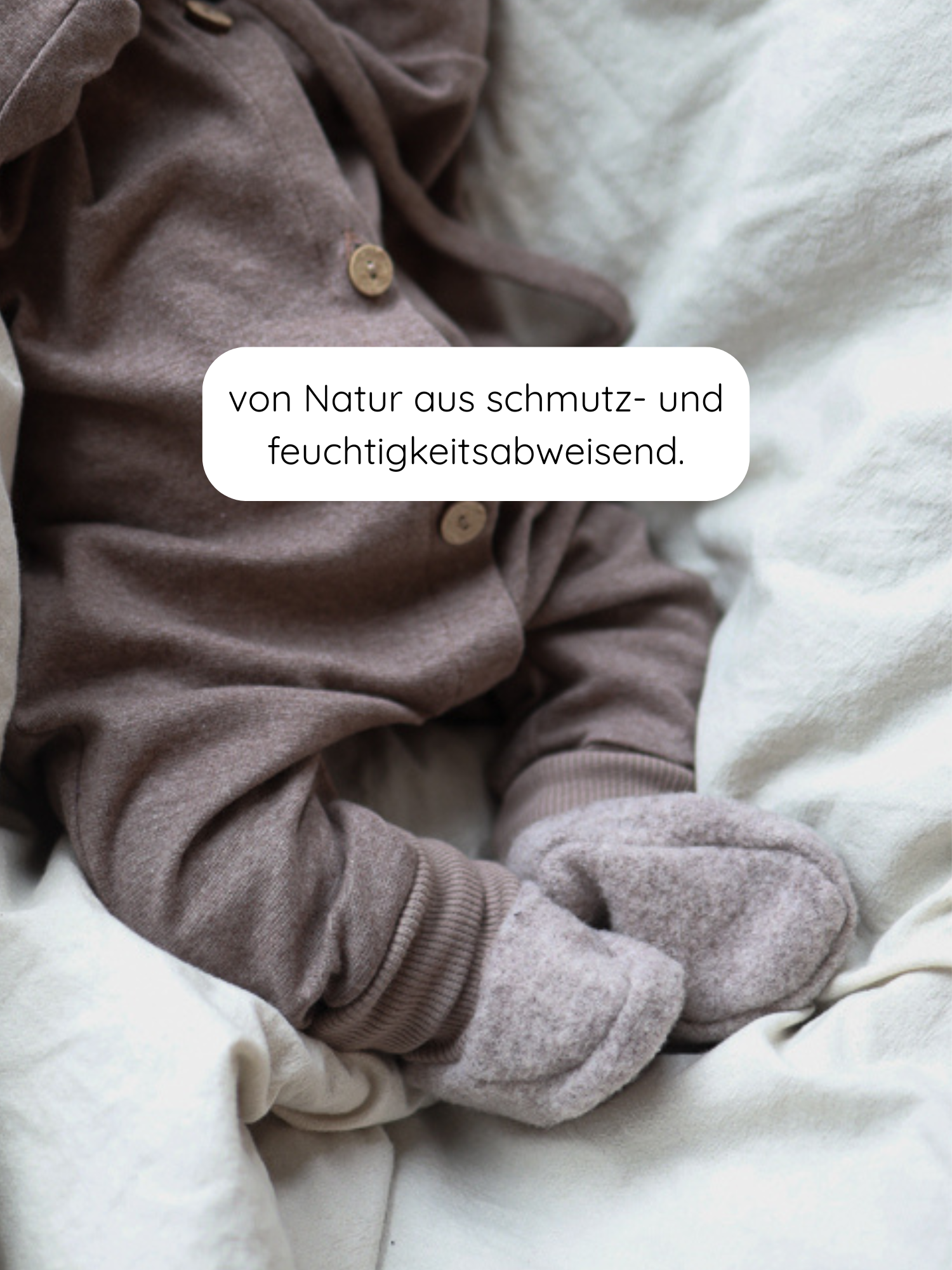 Babybooties Merino Wollfleece - Hafer: Ein Baby trägt weiche, braun-graue Merino-Wollfleece-Booties mit Holzknöpfen. Die Booties sind leicht, flexibel und passen sich an, ideal für wärmende, atmungsaktive Gemütlichkeit.