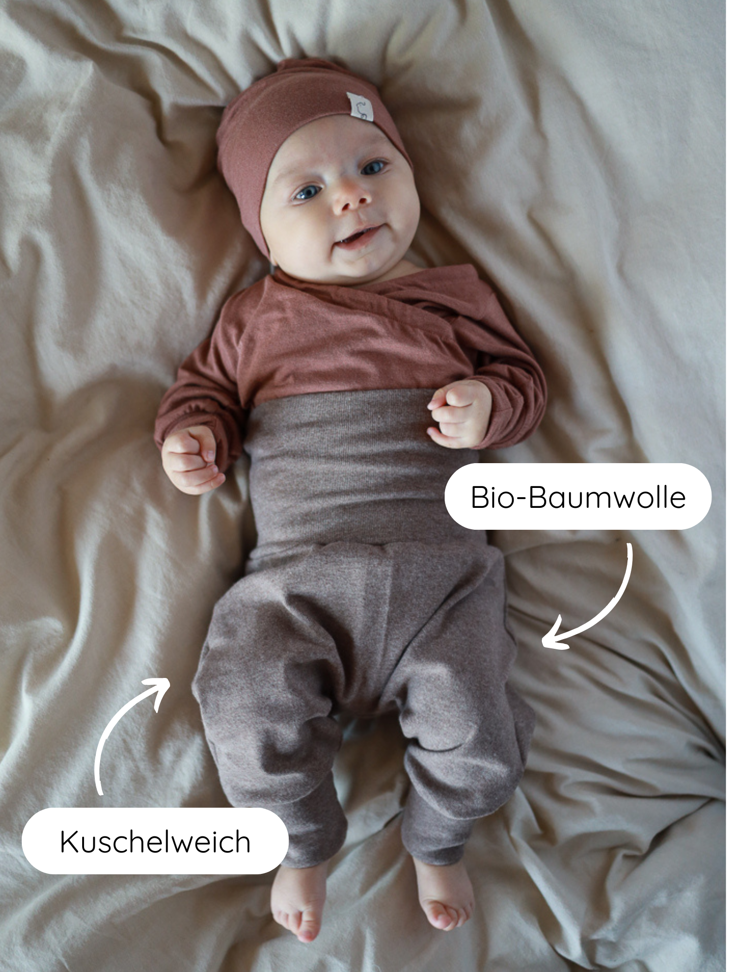 Babyknicker Feinstrick - Praline Meliert: Ein Baby liegt auf einer neutralen Oberfläche, gekleidet in erdigen Tönen. Labels zeigen auf das Bio-Baumwolle-Outfit, das kuschelweich und atmungsaktiv ist.
