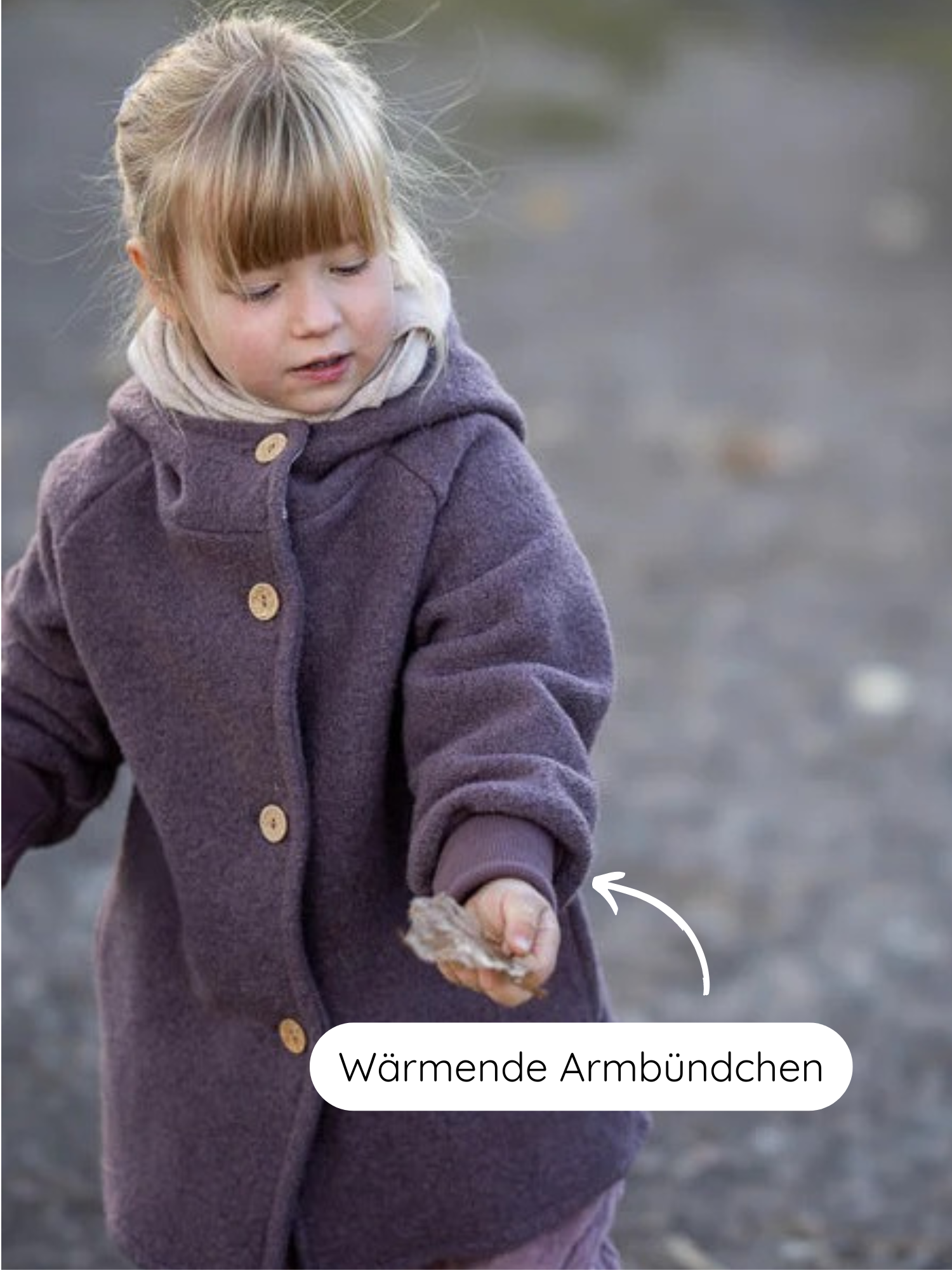 Kind im Freien trägt Wichteljacke Wollwalk - Malve mit Kapuze und Holzknöpfen, hält Blatt. Grafik zeigt Wärmende Armbündchen an den Ärmeln.