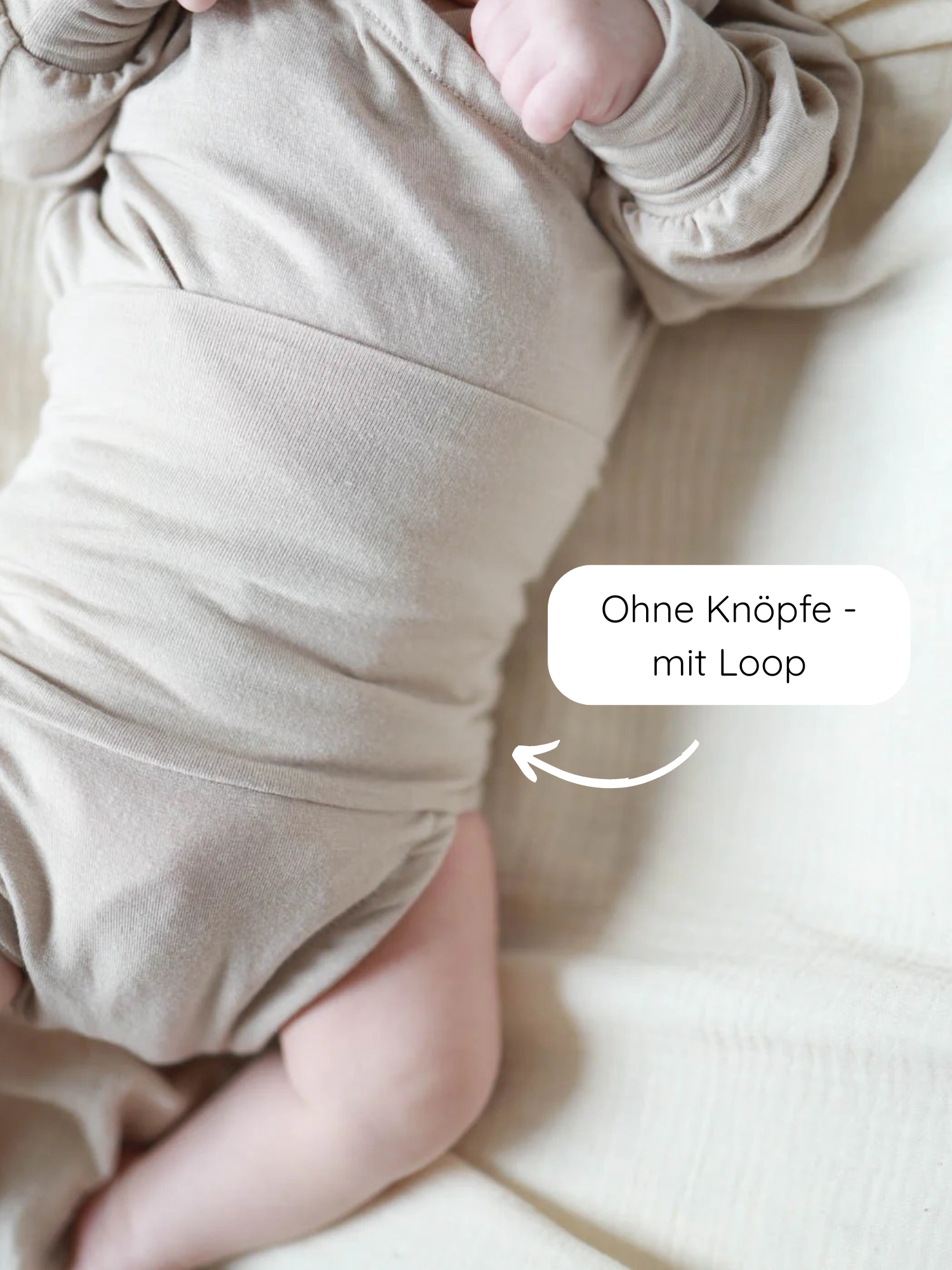 Ein Baby liegt auf einer cremefarbenen Decke, trägt den Loopbody Kaschmir-Mix - Sand in Beige, langärmelig, ohne Knöpfe, mit Schlaufe um den Bauch für einfaches Anziehen.