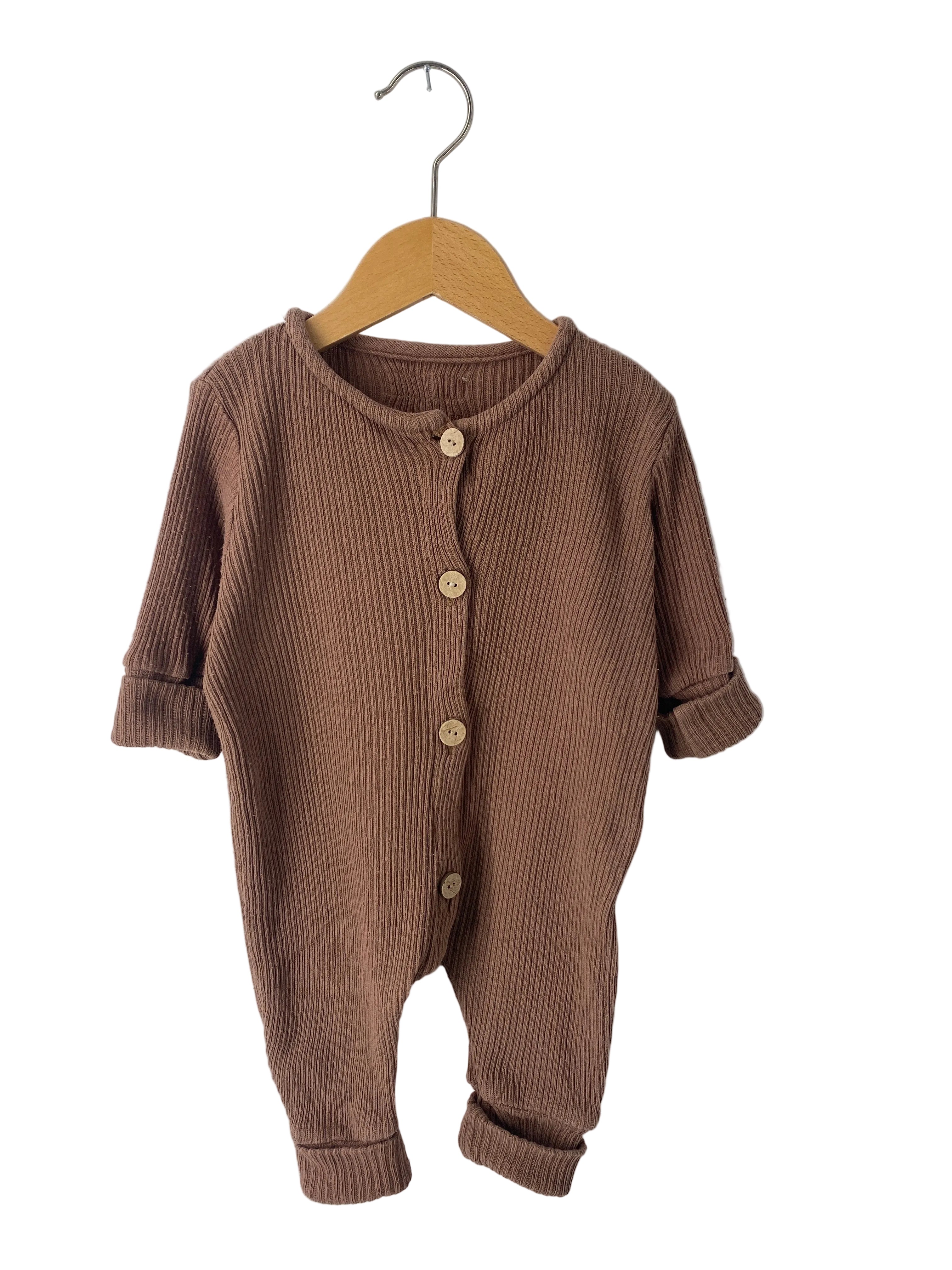 Kopie Mini Overall Rippstrick Nougat Gr 3M: Ein kleiner, langärmeliger Einteiler für Kleinkinder aus braunem Rippstrickstoff, vorne mit vier holzfarbenen Knöpfen zu schließen, an Holzkleiderbügel präsentiert. Zustand: gut.