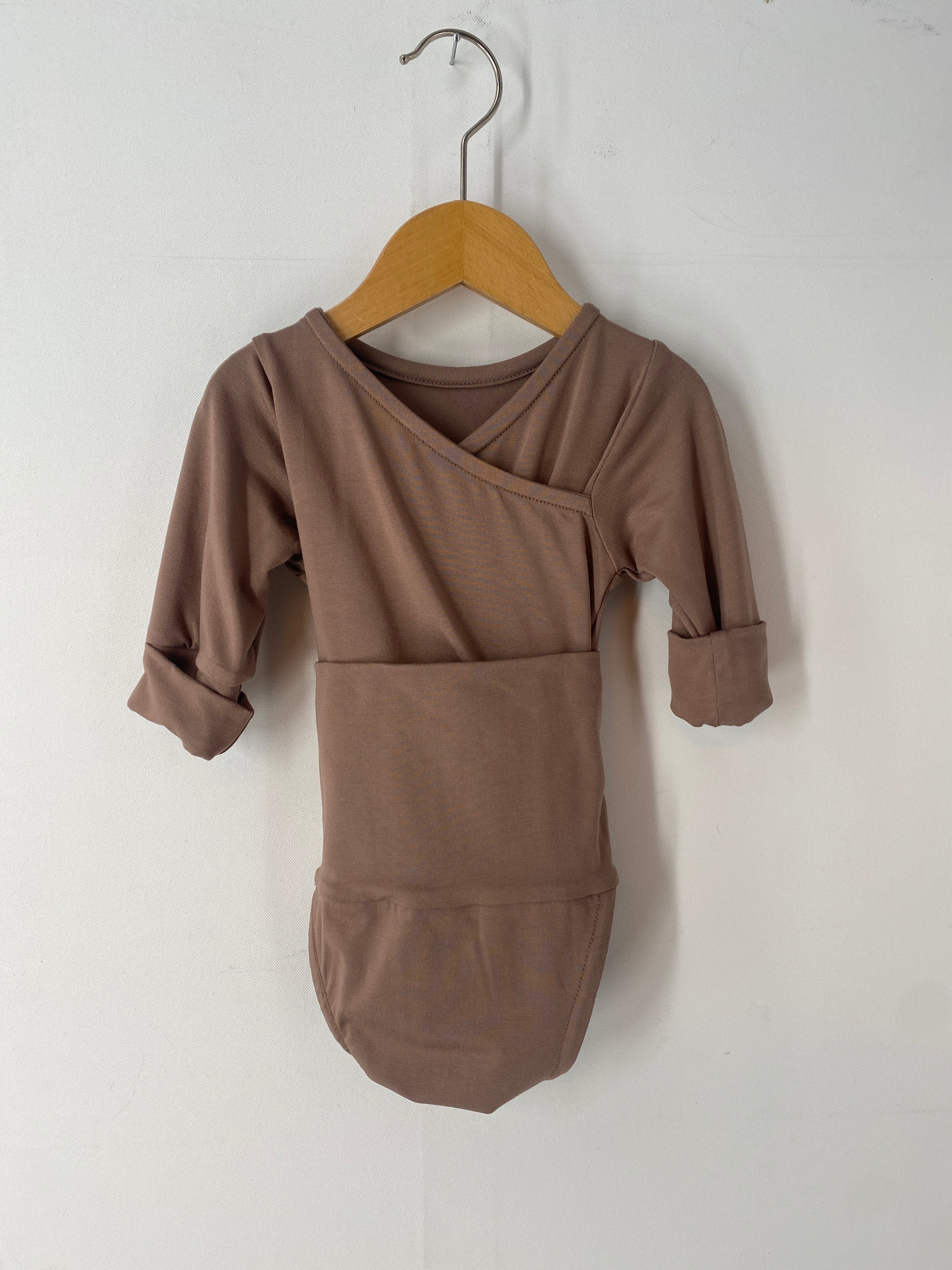 NEU Loopbody Bio-Baumwolle Praline Gr 0M auf einem Holzschwinger, sichtbar ist ein brauner Babybody mit Tasche.