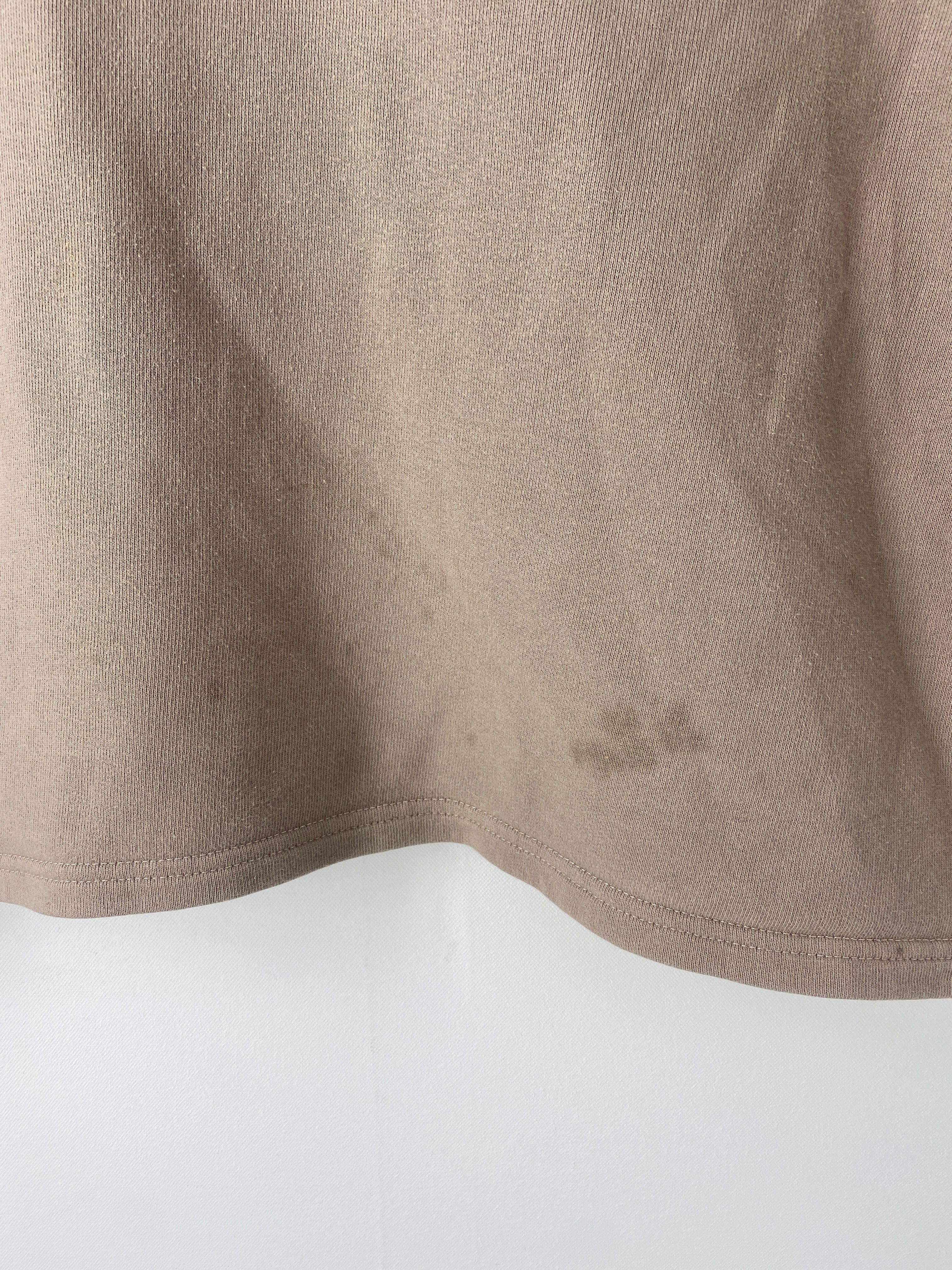 Kopie Frauen Pulli Bio Sweat Stein mit V-Ausschnitt Gr M/L, zeigt unterem Teil eines beigefarbenen T-Shirts mit Saumnaht, kleine dunkle Flecken sichtbar über dem Saum. Zustand: ok, Flecken unten/vorne.