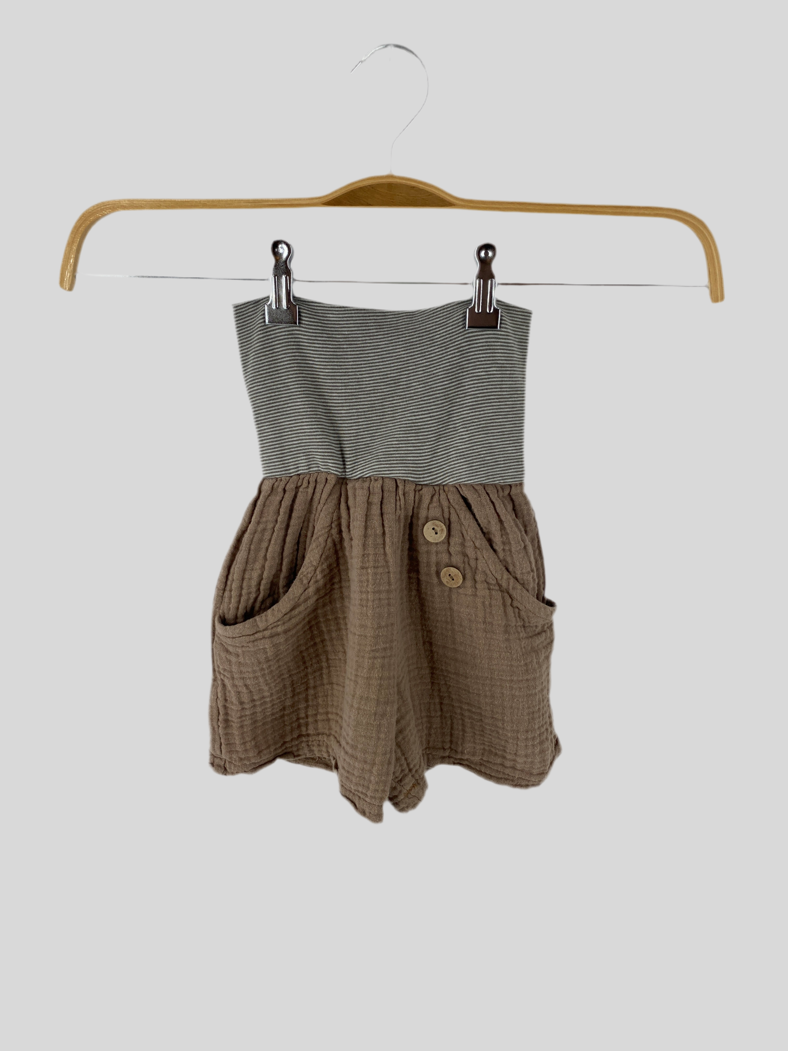 Kleinkind-Romper Kurze Buxe Musselin Praline Gr 2/3Y: Ärmelloses Design mit grau-weiß gestreiftem Tube-Top-Bodice und lockerem, strukturierem braunem Unterteil, dekoriert mit zwei vorderen Taschen und runden Holzknöpfen.