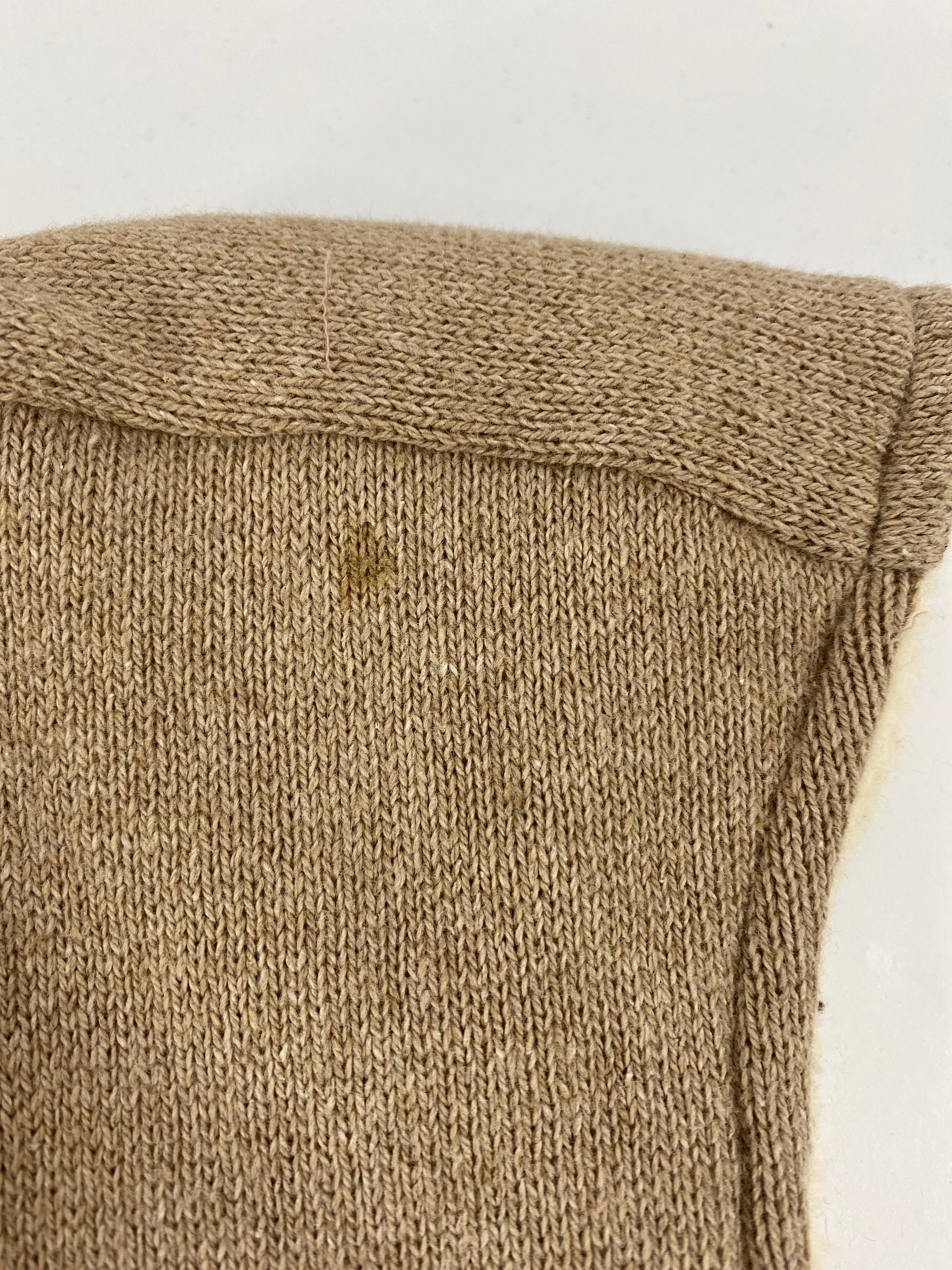 Nahaufnahme des Babyhäubchens Strick Hafer mit Teddy Gr 6M. Das Bild zeigt einen Abschnitt des Kleidungsstücks mit einem kleinen dunkleren Fleck auf dem gestrickten Stoff. Zustand: neu.