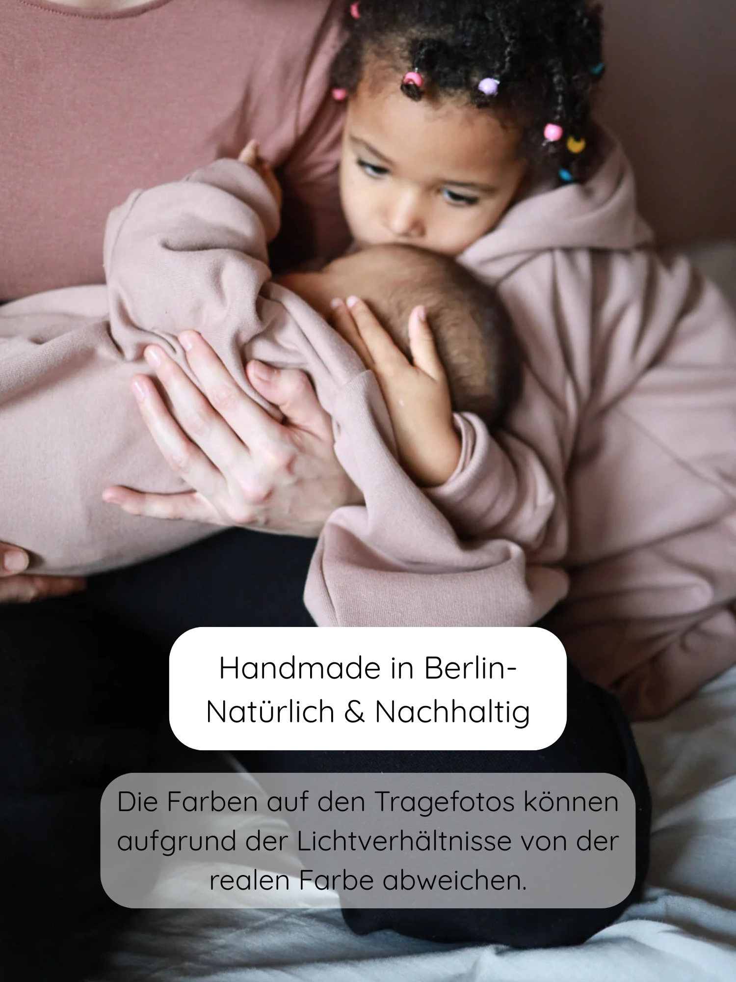 Elternteil hält Baby, während älteres Kind in passendem Outfit den Kopf küsst. Der Kuschelanzug Bio-Sweat - Puder, handgemacht in Berlin, ist weich und nachhaltig.