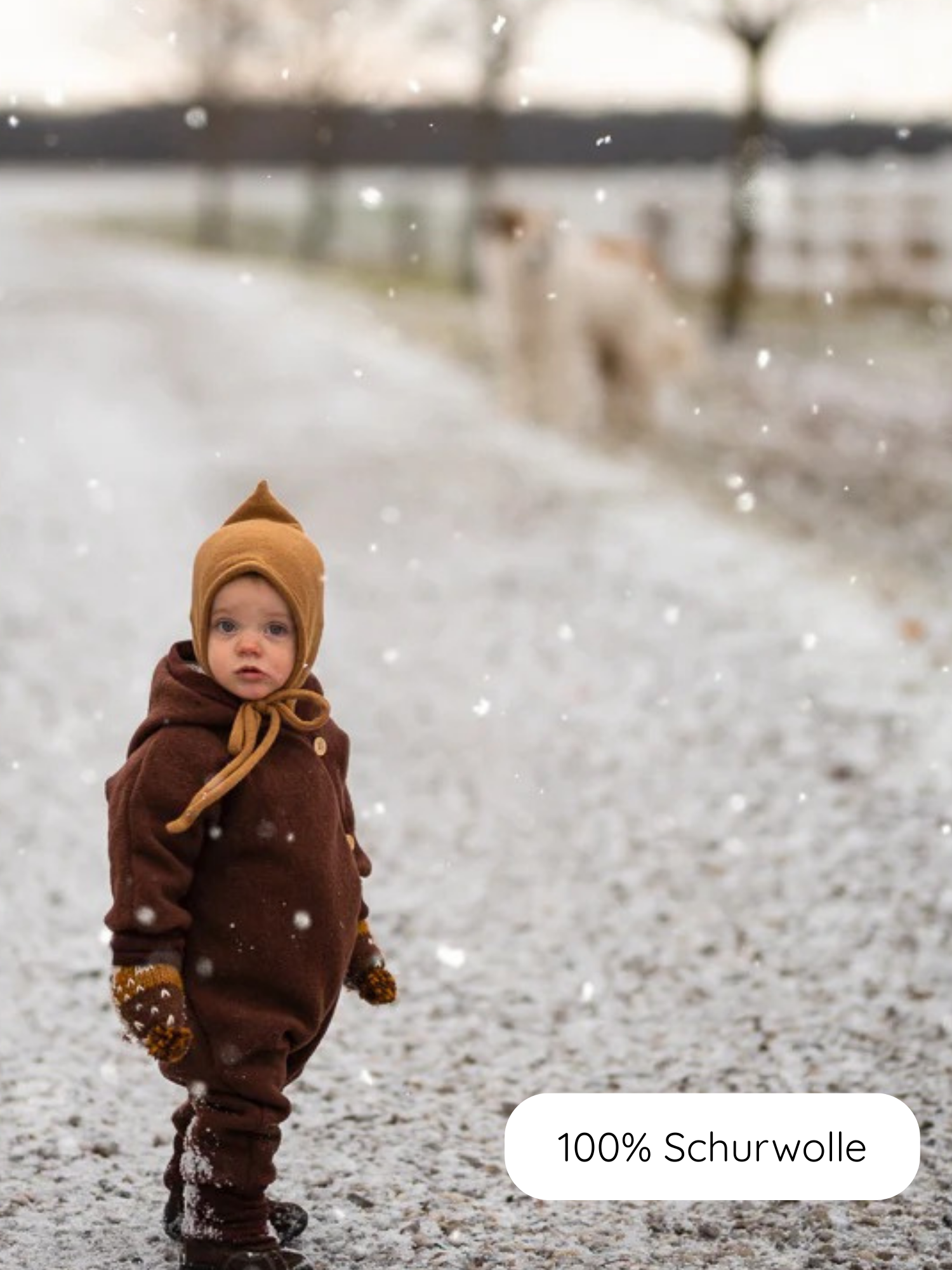 Kind in warmem Winter Wollwalk Overall mit Teddyfutter - Schoko, aus 100% Schurwolle. Perfekt für kalte Tage, mit Kapuze und Fäustlingen, auf schneebedecktem Weg stehend.