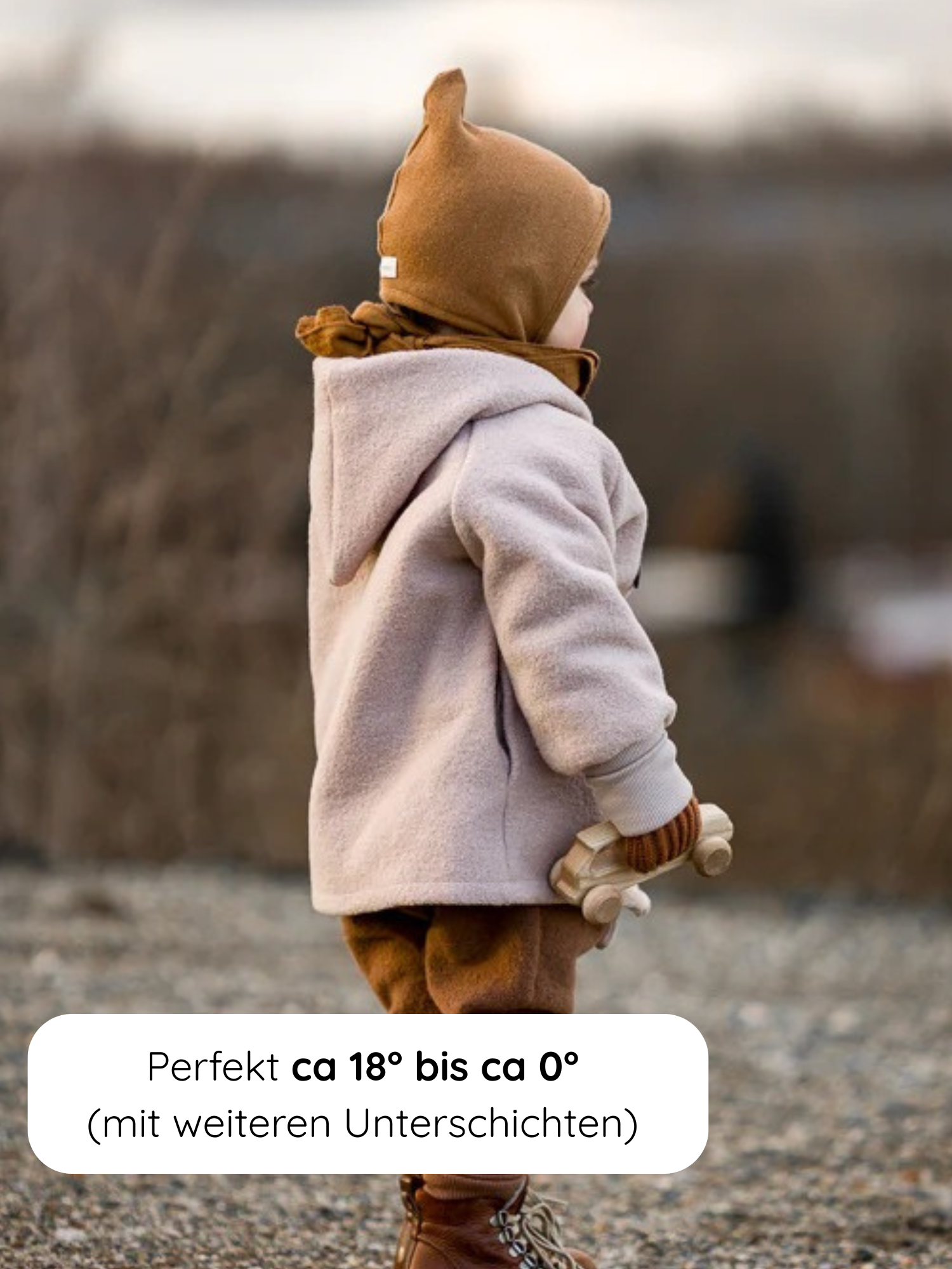 Ein Kleinkind im Profil trägt die Wichteljacke Wollwalk - Sand, mit Kapuze und krempelbaren Bündchen, perfekt für kühles Wetter. In der Hand hält es ein schlichtes Holzauto.
