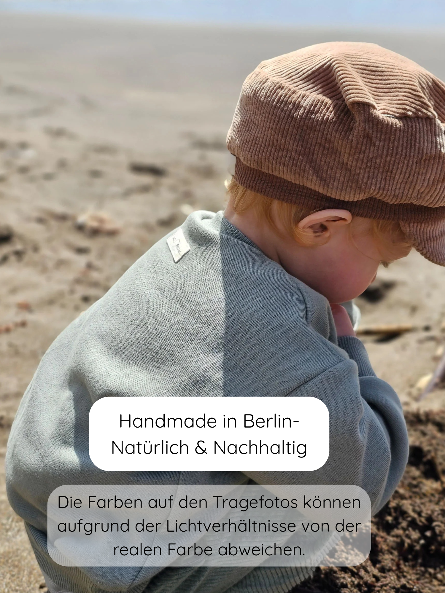 Kind von hinten am Strand, trägt Pulli Bio-Sweat - Aqua und eine Cordmütze. Der Pulli zeigt fair gefertigte Bio-Qualität aus Berlin, ideal für Alltag und Spiel.