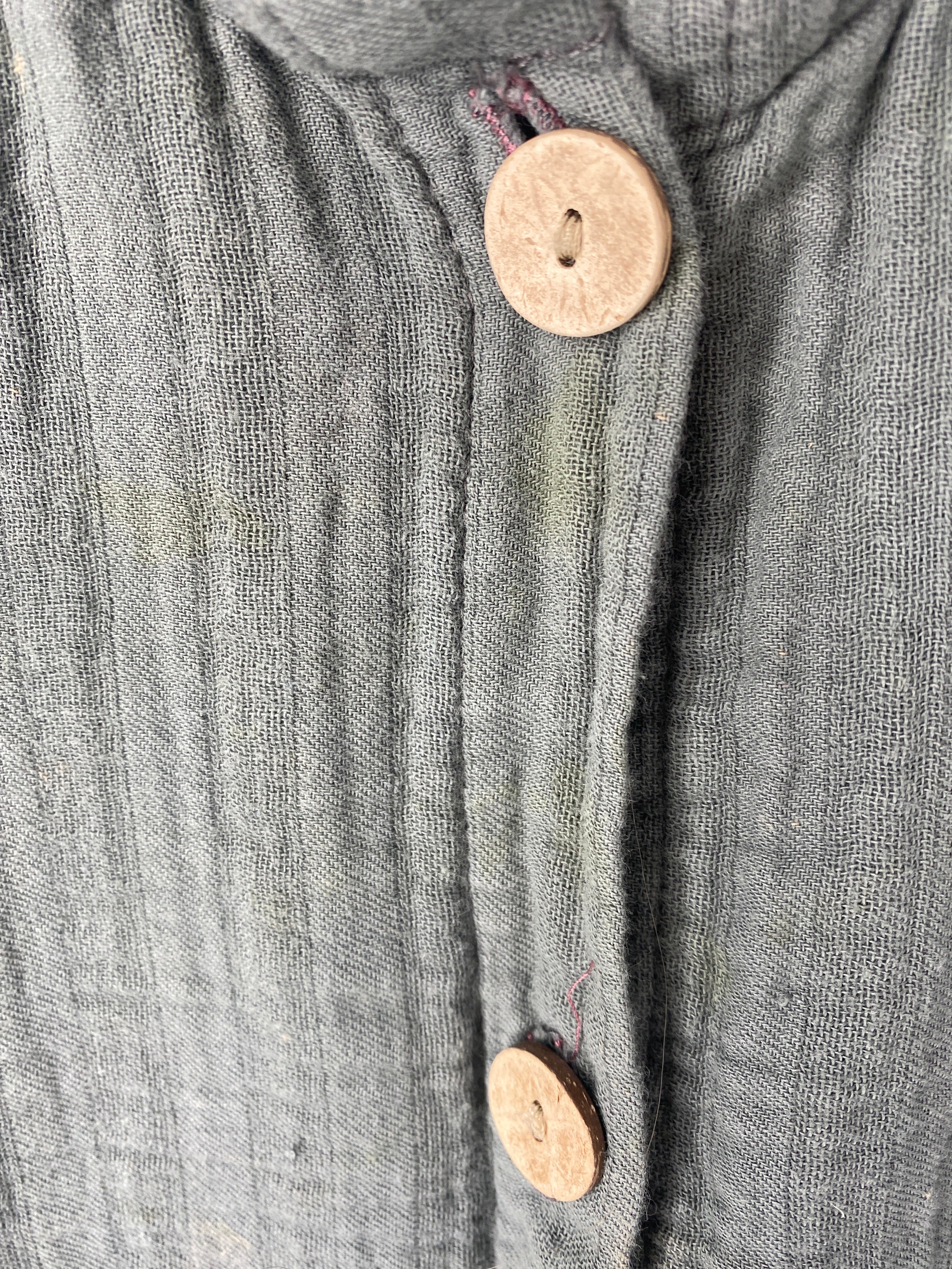Nahaufnahme des Mini Overall Musselin Taube Gr 2Y, zeigt die Vorderseite mit locker gewebtem Stoff und zwei runden, hellen Holzknöpfen. Zustand: gut, mit leichten Flecken.