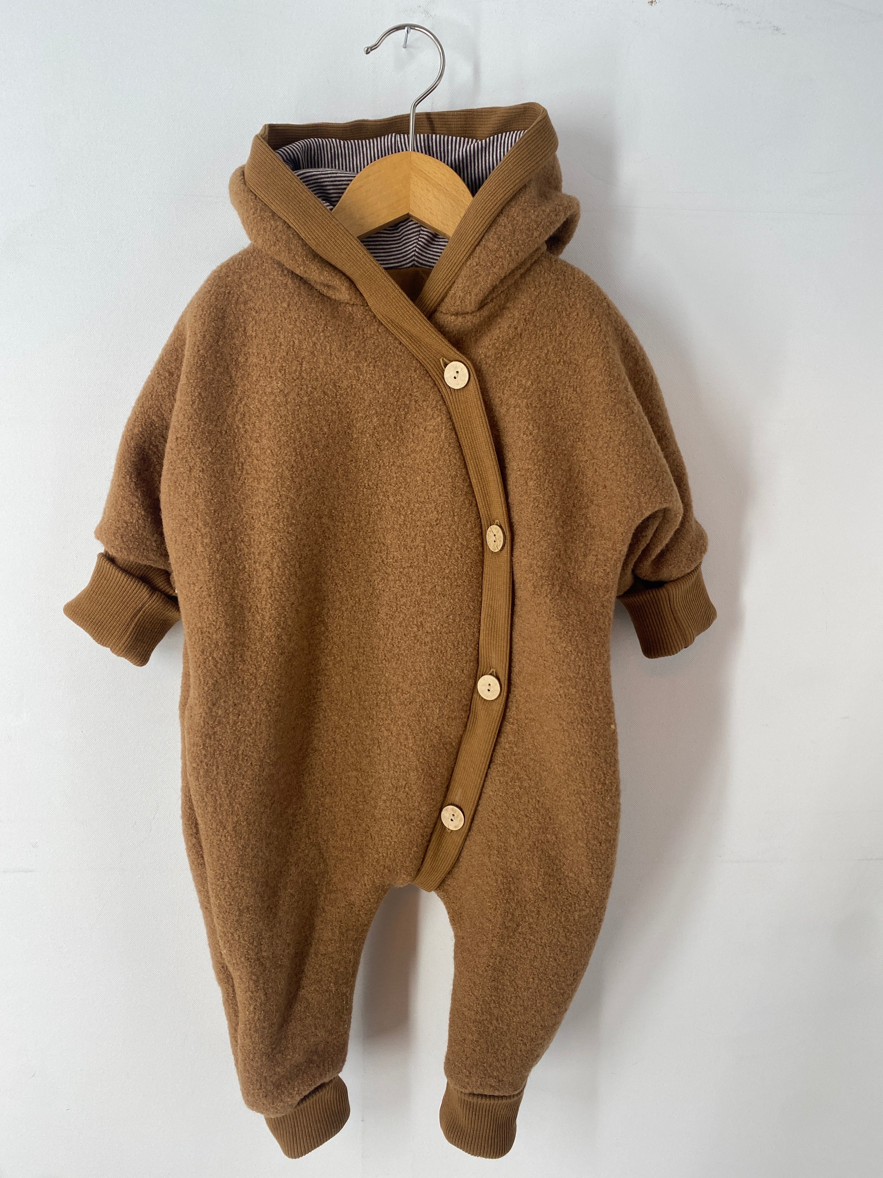 NEU Kuschelanzug Wollwalk Sahara Gr 6M auf einem Schwinger präsentiert, zeigt feine Strickdetails und Knöpfe, ideal für Babys.