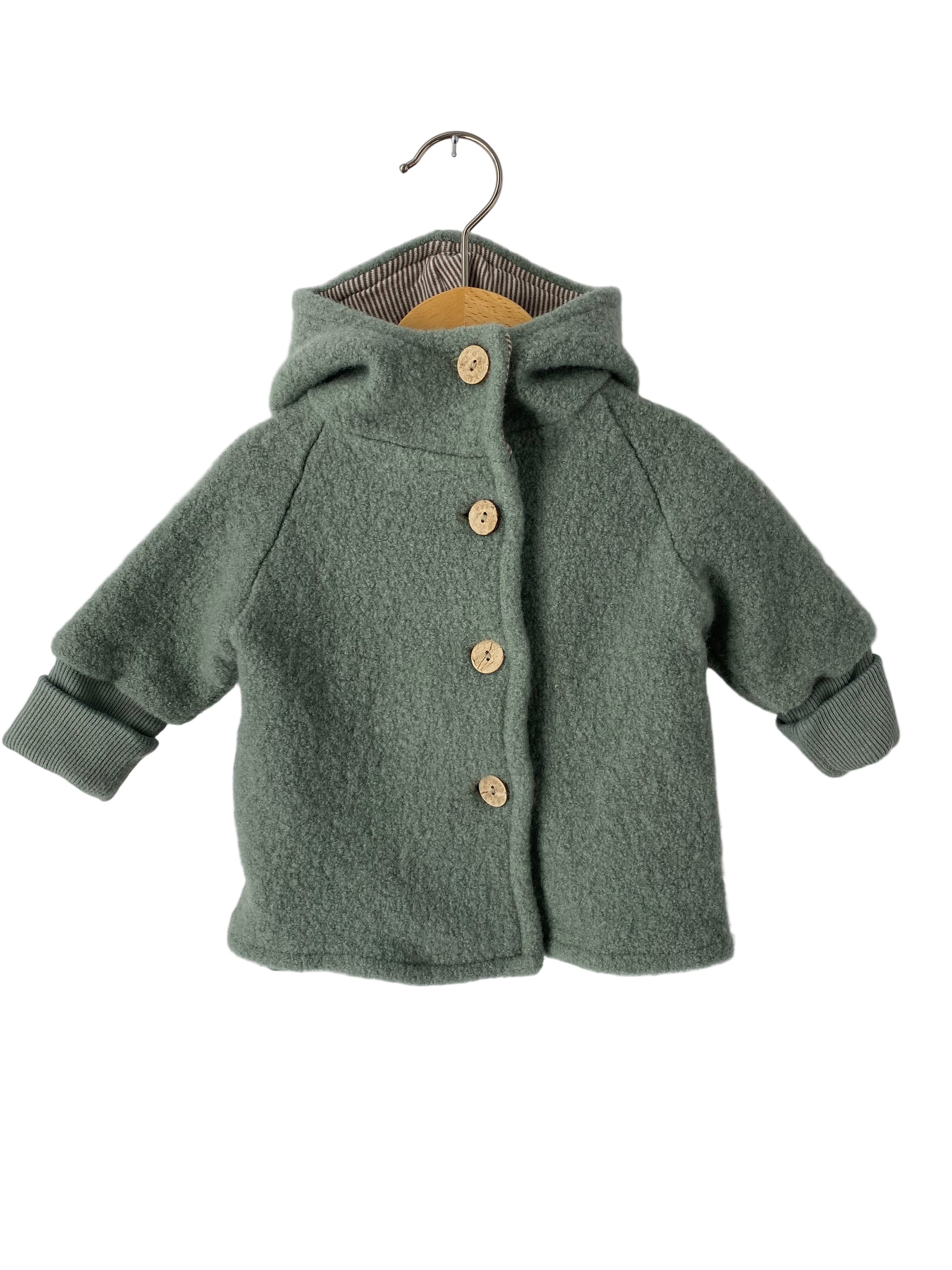 (Kopie) Wichteljacke Wollwalk Aqua Gr 6M: Kleiner Kapuzenmantel für Babys aus Wollmischung mit langen Raglanärmeln, gerippten Bündchen und vier Holzknöpfen, präsentiert auf einem Holzkleiderbügel vor weißem Hintergrund.