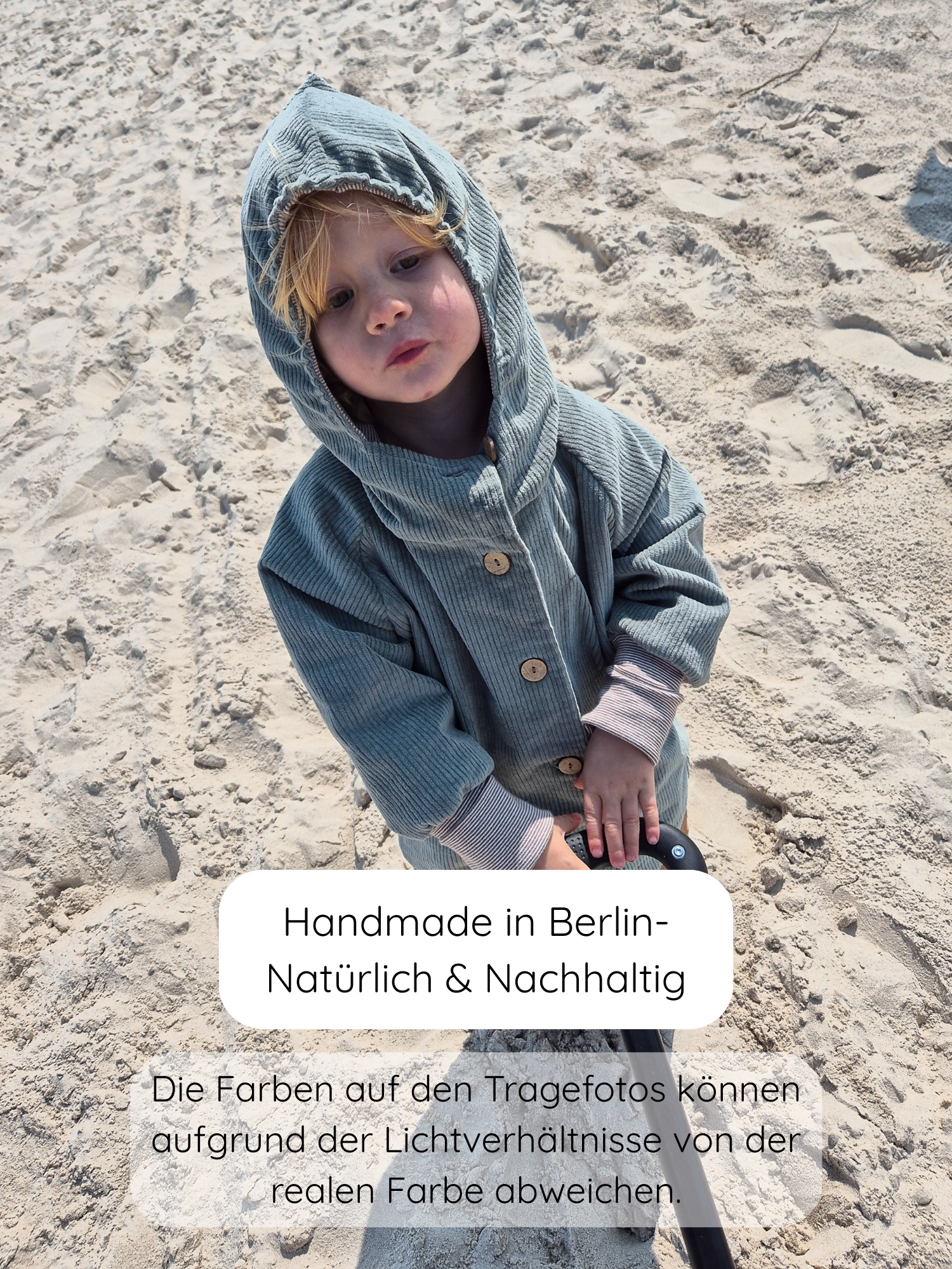 Ein Kind steht auf Sand, trägt die Wichteljacke Breitcord Stretch-Aqua mit Wichtelkapuze, hält einen Griff. Handgefertigt in Berlin, bietet die Jacke komfortablen Sitz und wächst dank krempelbarer Bündchen mit.