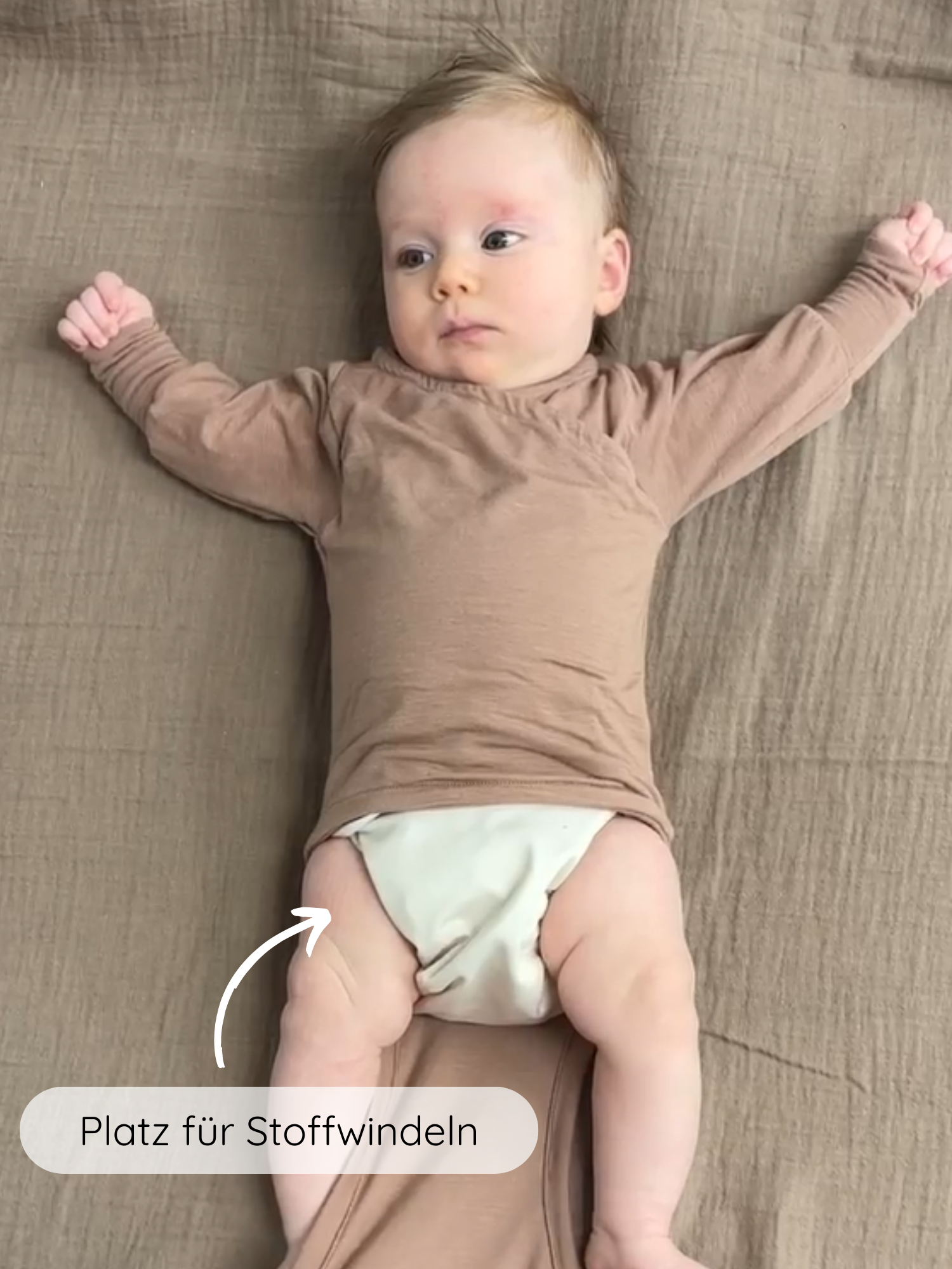 Baby in einem Loopbody Kaschmir-Mix - Puder mit langen Ärmeln und weichen Fold-over-Manschetten, tragend über einer Stoffwindel. Ein Pfeil zeigt auf den Windelbereich mit Hinweis Platz für Stoffwindeln.