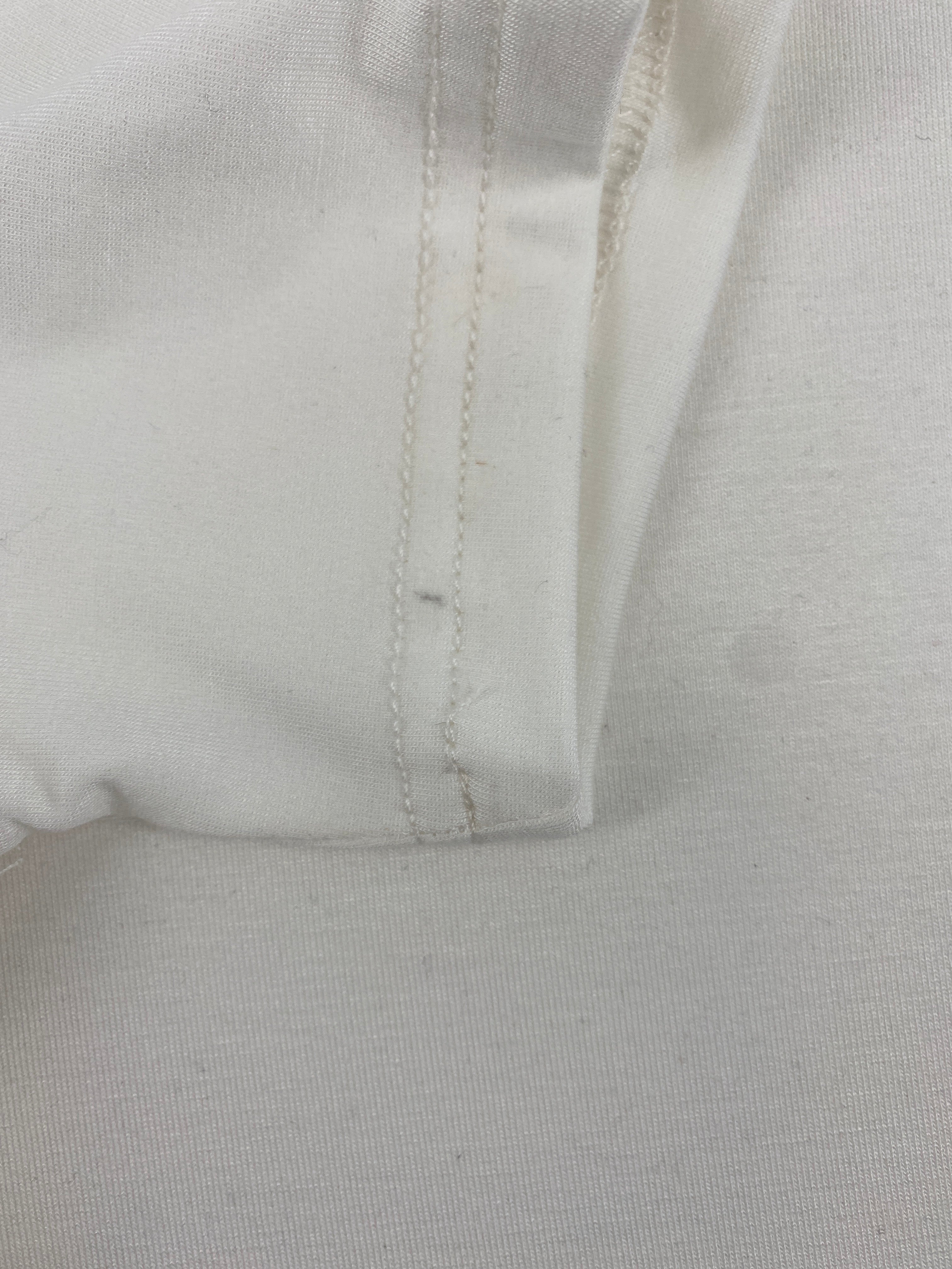 Nahaufnahme des Kurzarm Loopbody Bambusviskose Natur Gr 1Y, zeigt eine doppelt genähte Naht am Saum. Sichtbare kleine Flecken am Ärmel, die den neuen Zustand des Kleidungsstücks minimal beeinträchtigen.