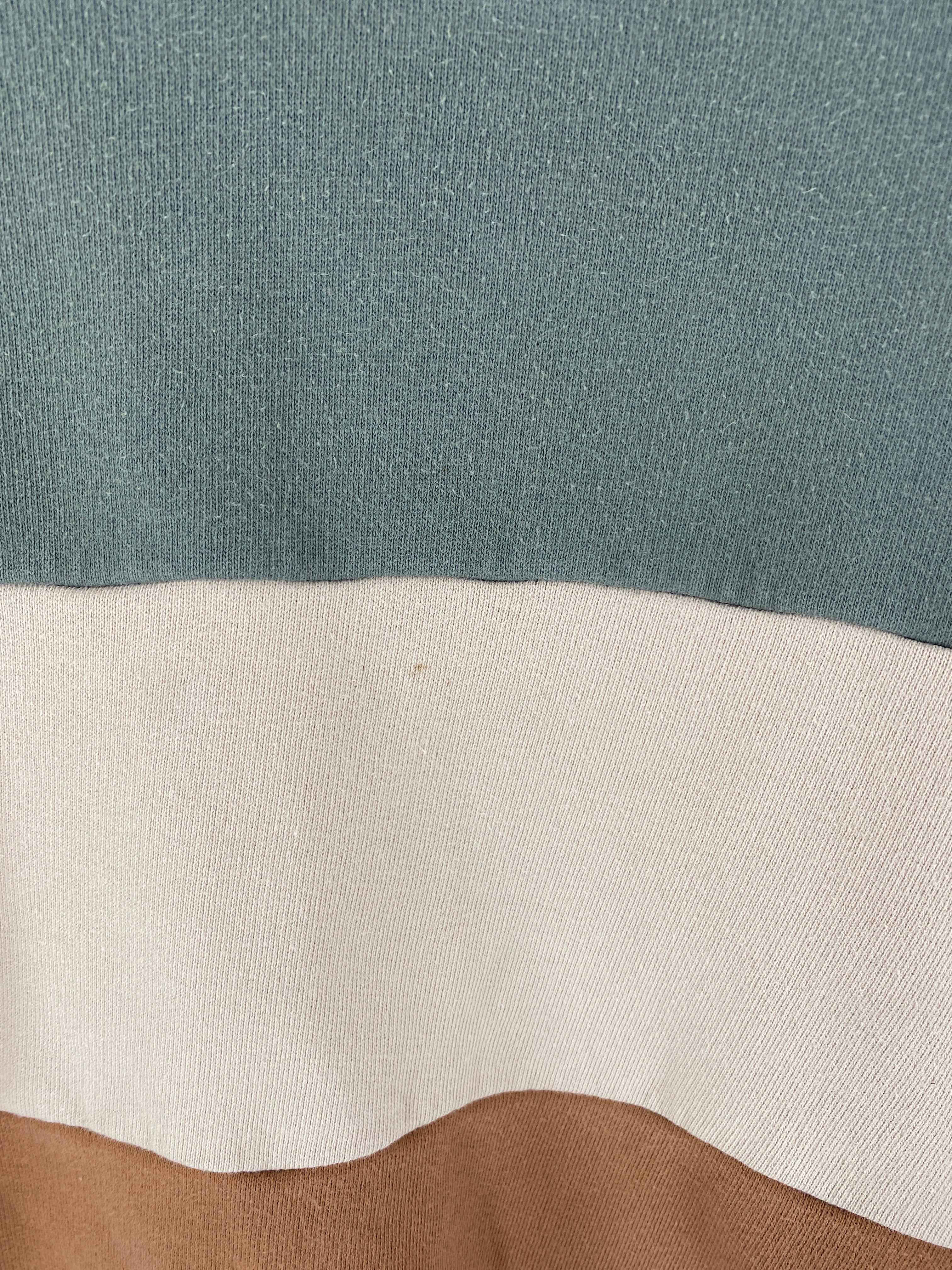 Nahaufnahme von Kopie Streifenpulli Bio Sweat Taube/Marine Gr 8/9, zeigt horizontal gestrickte Farbblöcke mit einem kleinen Fleck vorne; Farben: gedämpftes Grün, Off-White, Hellbraun. Zustand: gut.