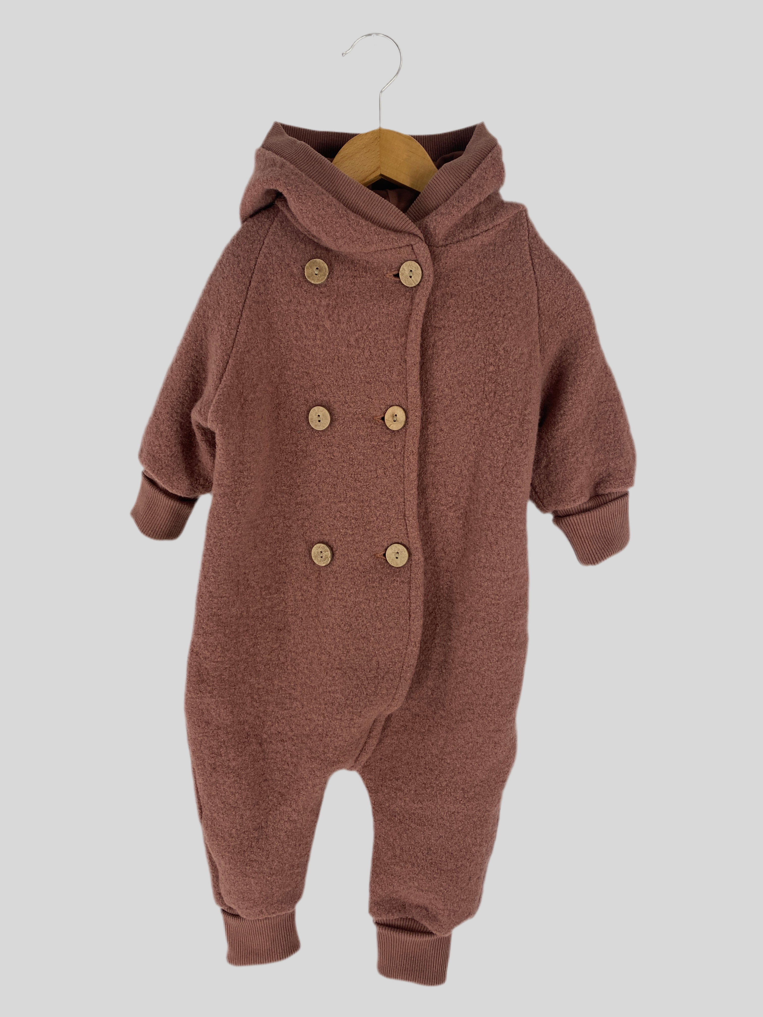 Zweireiher Wollwalkanzug Zimt Gr 6M auf einem Schaukelstuhl mit Knöpfen, ergänzt durch eine braune Strickmütze, präsentiert als gemütliche und stilvolle Babybekleidung. Zustand: sehr gut.