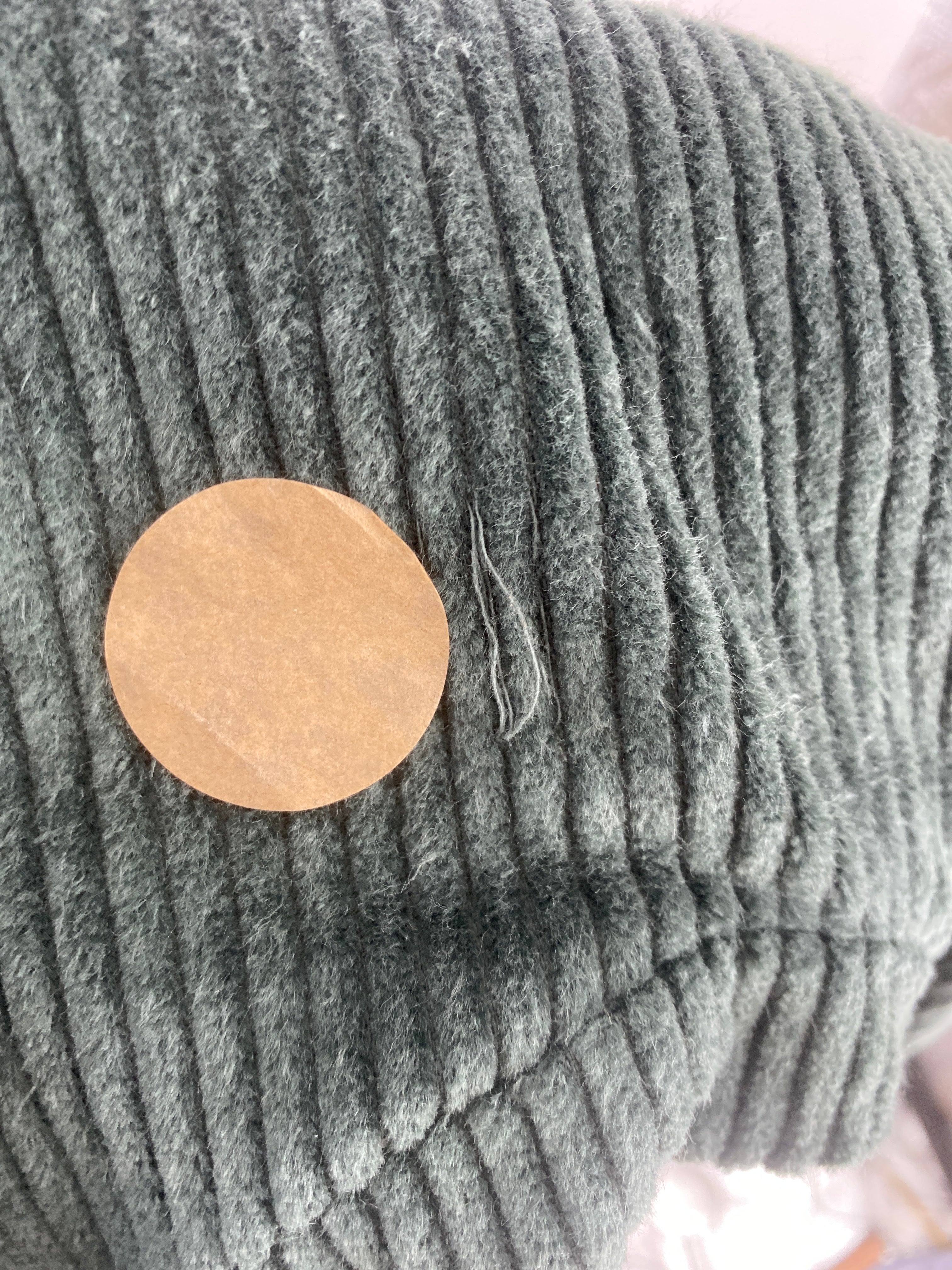 Nahaufnahme des Knickerbocker Breitcord Jade Gr 3Y: Gerippter Stoff mit braunem Aufkleber und vereinzelten Fasern, Zustand neu, jedoch mit Stofffehler vorne.