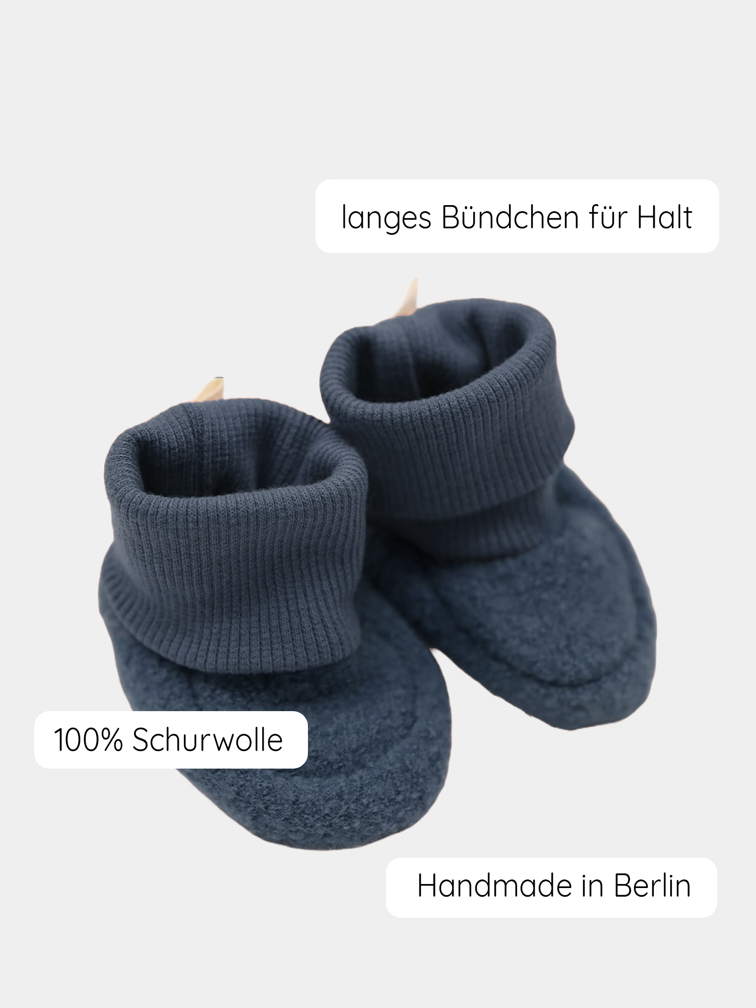 Babybooties Wollwalk - Marine: Dunkelblaue, handgestrickte Babybooties aus 100 % Schurwolle mit langem, geripptem Bündchen für sicheren Halt. Etiketten weisen auf Handmade in Berlin und 100 % Schurwolle hin.