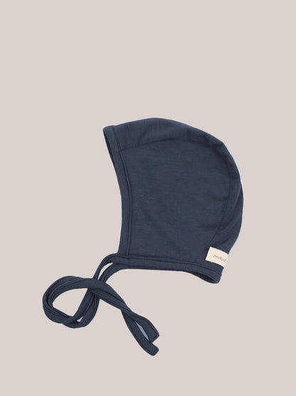 Babyhäubchen Kaschmir-Mix - Blaubeere: Ein weiches, navy-blaues Babyhäubchen mit langen Stoffbändern zum Binden, aus elastischem Micromodal-Kaschmirstoff, ideal für sanfte Wärme und Schutz, mit kleinem Seitenschild.