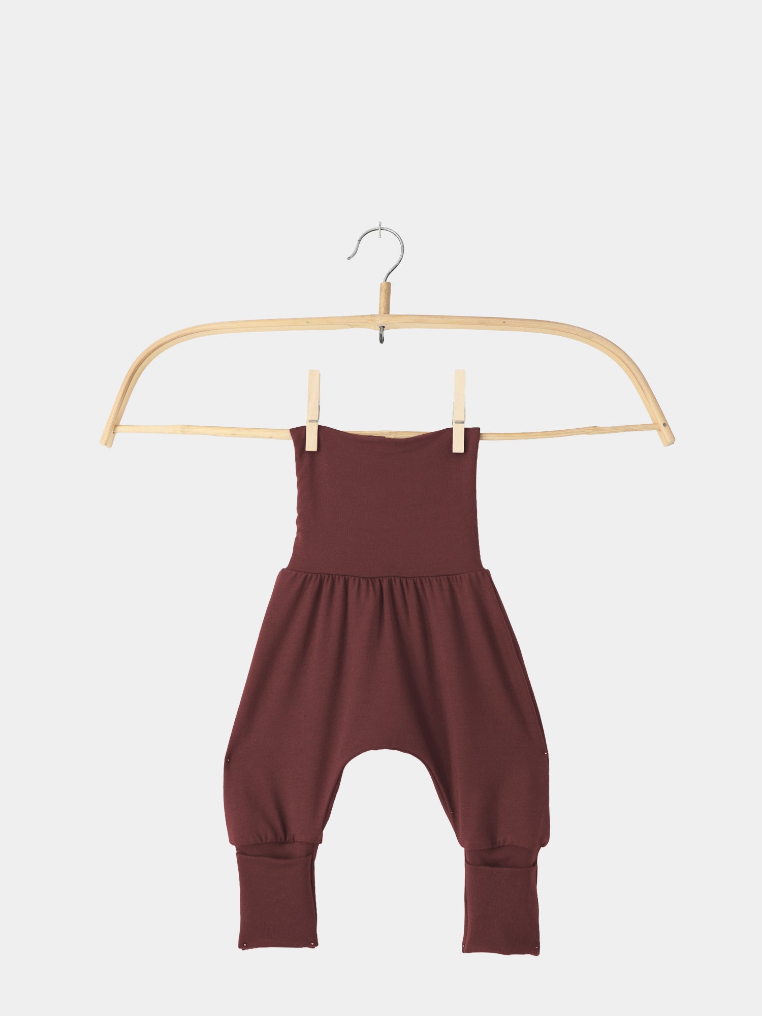 Babyknicker Bambusviskose - Burgund: Ein burgunderfarbener Baby-Harem-Overall aus weicher, atmungsaktiver Bambusviskose, aufgehängt an einem einfachen Holzbügel mit zwei Holzwäscheklammern. Ideal für Bewegungsfreiheit und Komfort.