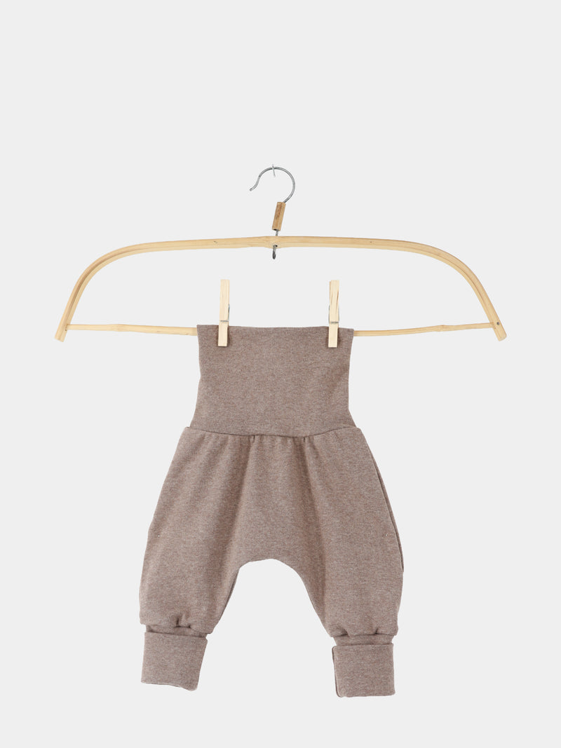 Babyknicker Feinstrick - Praline Meliert: Weiche, braune Babyhose aus elastischem Feinstrick-Jersey mit hohem Bund, tiefem Schnitt und schmalen Bündchen, aufgehängt an einem einfachen Holzbügel mit Metallhaken, vor weißem Hintergrund.