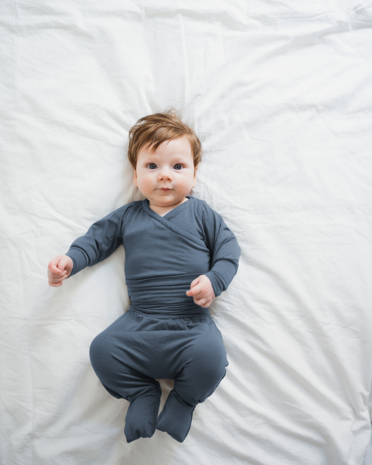 Baby in einem langärmligen, fußbedeckenden Einteiler in Blaubeere. Der Babyknicker Kaschmir-Mix - Blaubeere bietet Wärme und Komfort, ideal für zarte Babyhaut und perfekt für die ersten Lebenswochen.