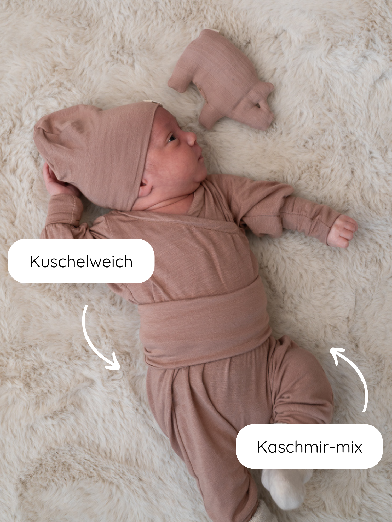 Neugeborenes auf weichem, weißen Plüschteppich, gekleidet in Babyknicker Kaschmir-Mix - Puder Set mit passendem Hut und Kuscheltier. Kuschelweich und Kaschmir-mix Labels verdeutlichen Qualität und Weichheit.