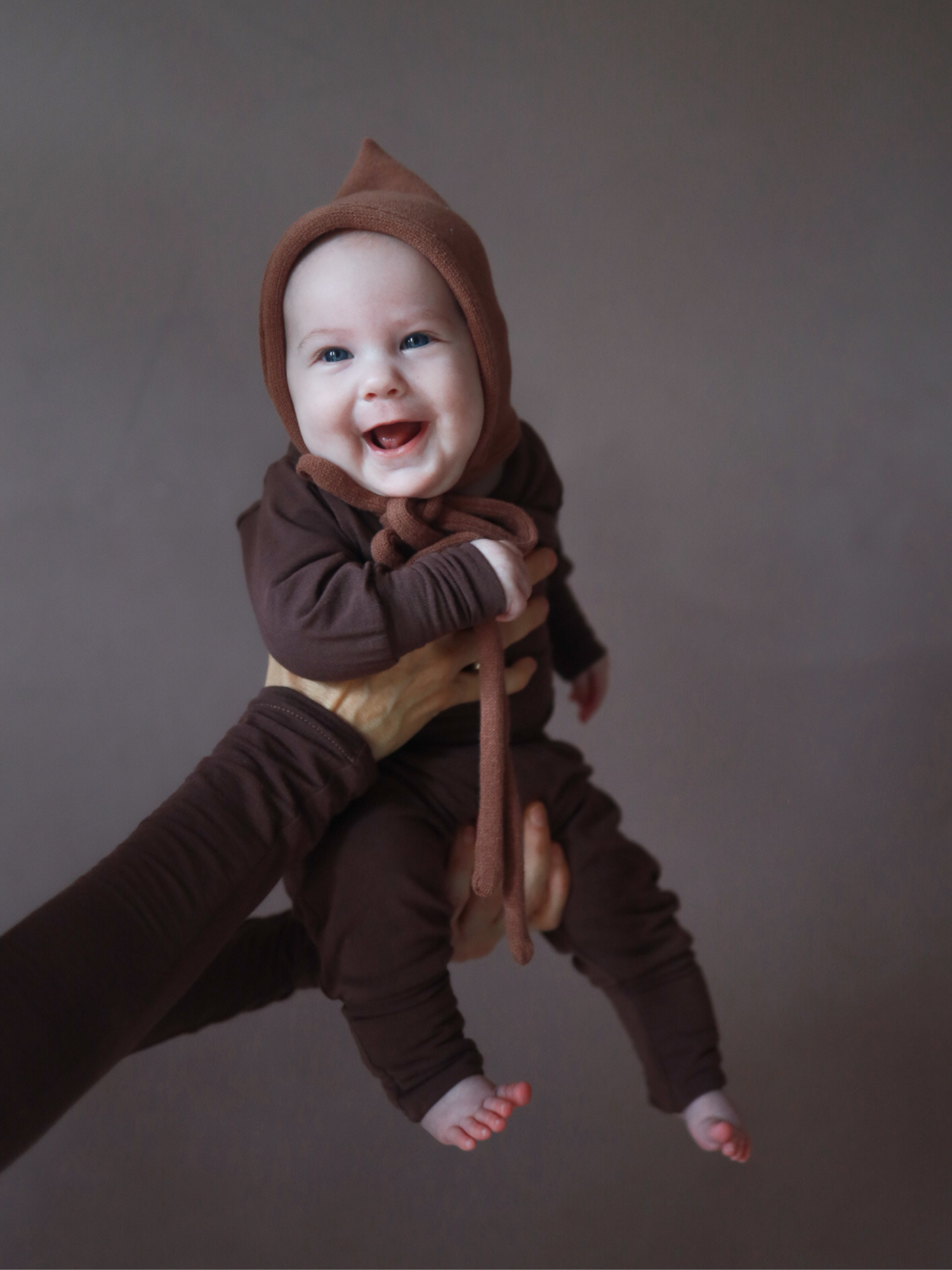 Ein lächelndes Baby trägt Babyknicker Kaschmir-Mix - Malve mit Klappbündchen und passendem Loopbody, gehalten von Erwachsenen, vor neutralem Hintergrund. Perfekt für weiche, wärmende Erstausstattung.