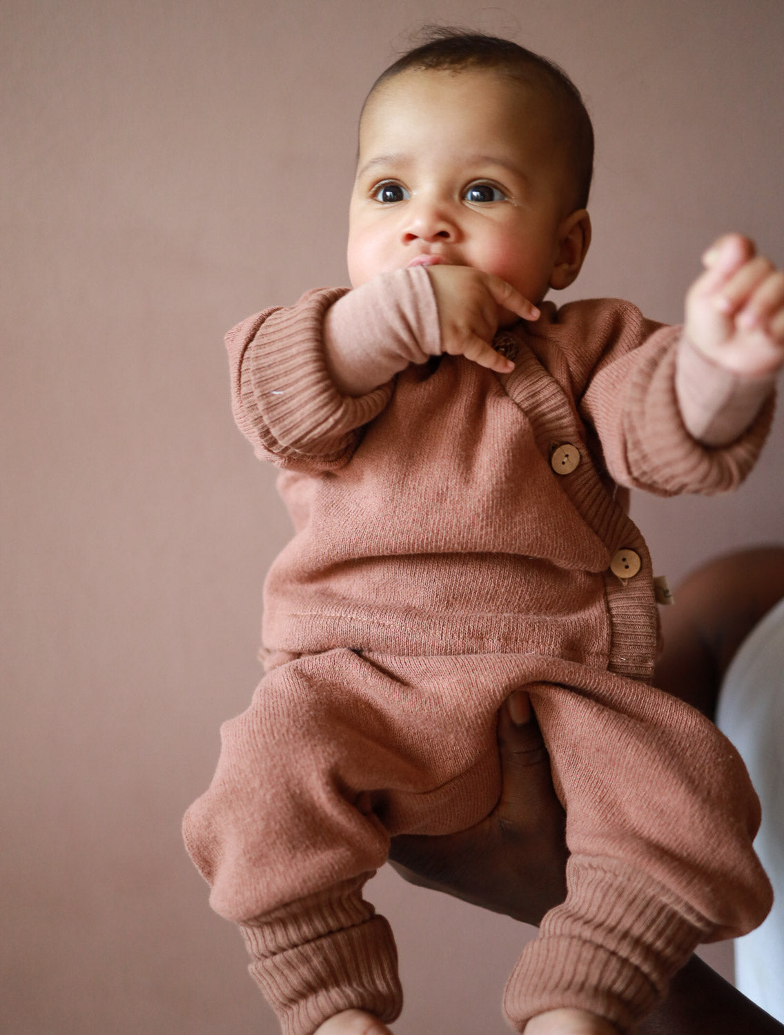 Babyschlüttli Strick - Nougat: Ein Baby in einem kuscheligen, braunen Strickoberteil aus recycelter Baumwolle, das bequem und langlebig für Jungen und Mädchen gestaltet ist. Erstausstattung Babys. Perfekte Baby Geschenke.