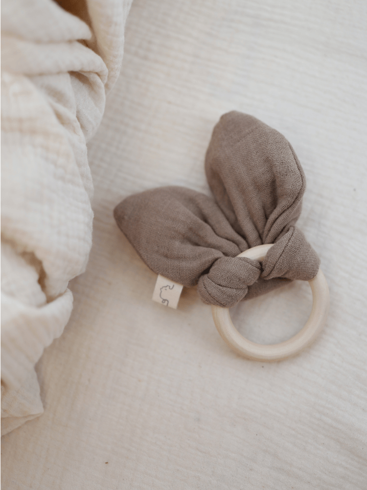 Baby Beißring Baumwoll-Musselin - Praline auf weichem Tuch. Holzring mit Musselin-Hasenohren, ideal für zahnende Babys und sensorische Entwicklung. Nachhaltig, handgefertigt, perfekt zum Greifen und Fühlen.